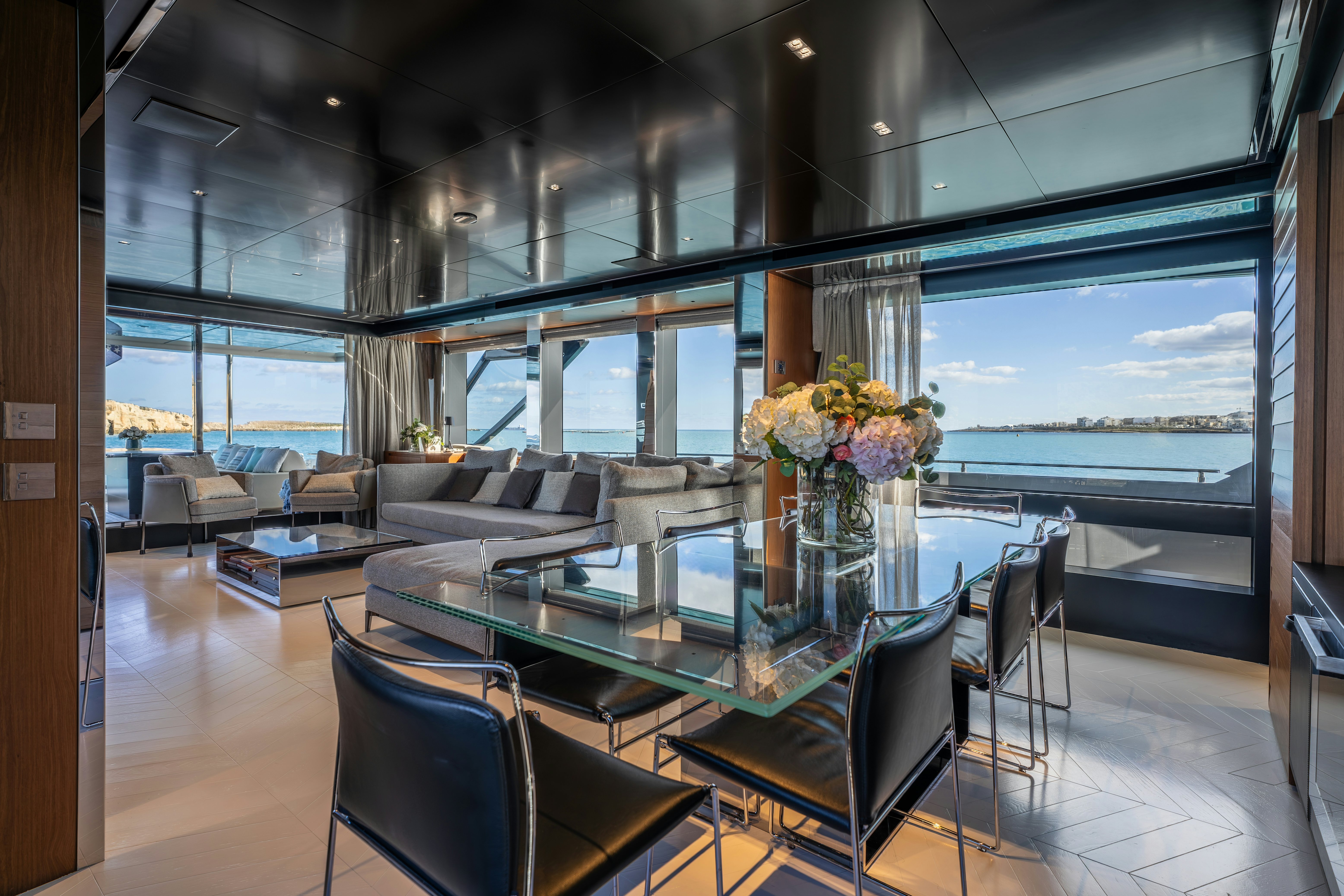 a living room with a large glass table and a view of the ocean aboard NOI Yacht for Sale