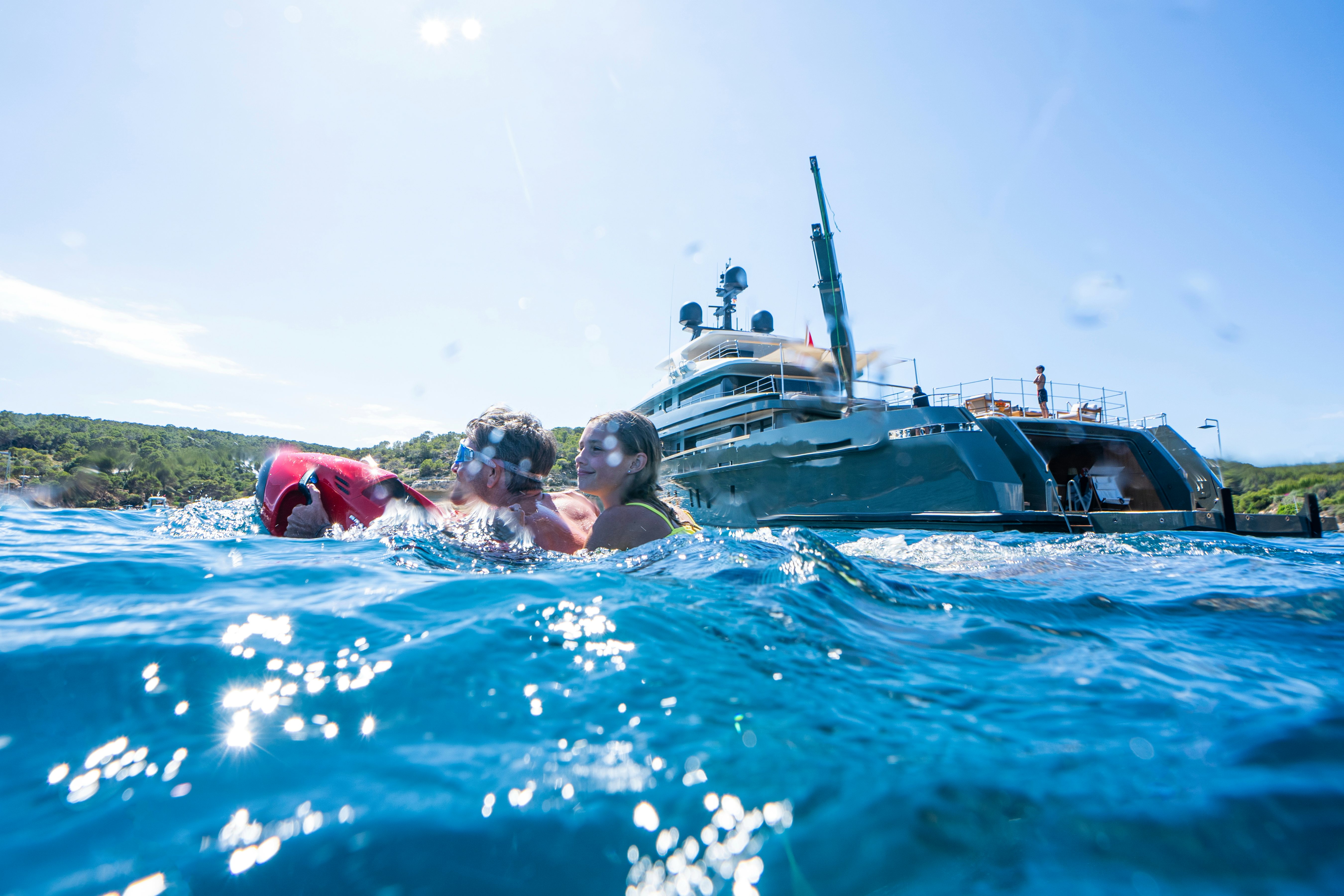 a group of people swimming in a body of water with a boat in the background aboard MOKA Yacht for Charter