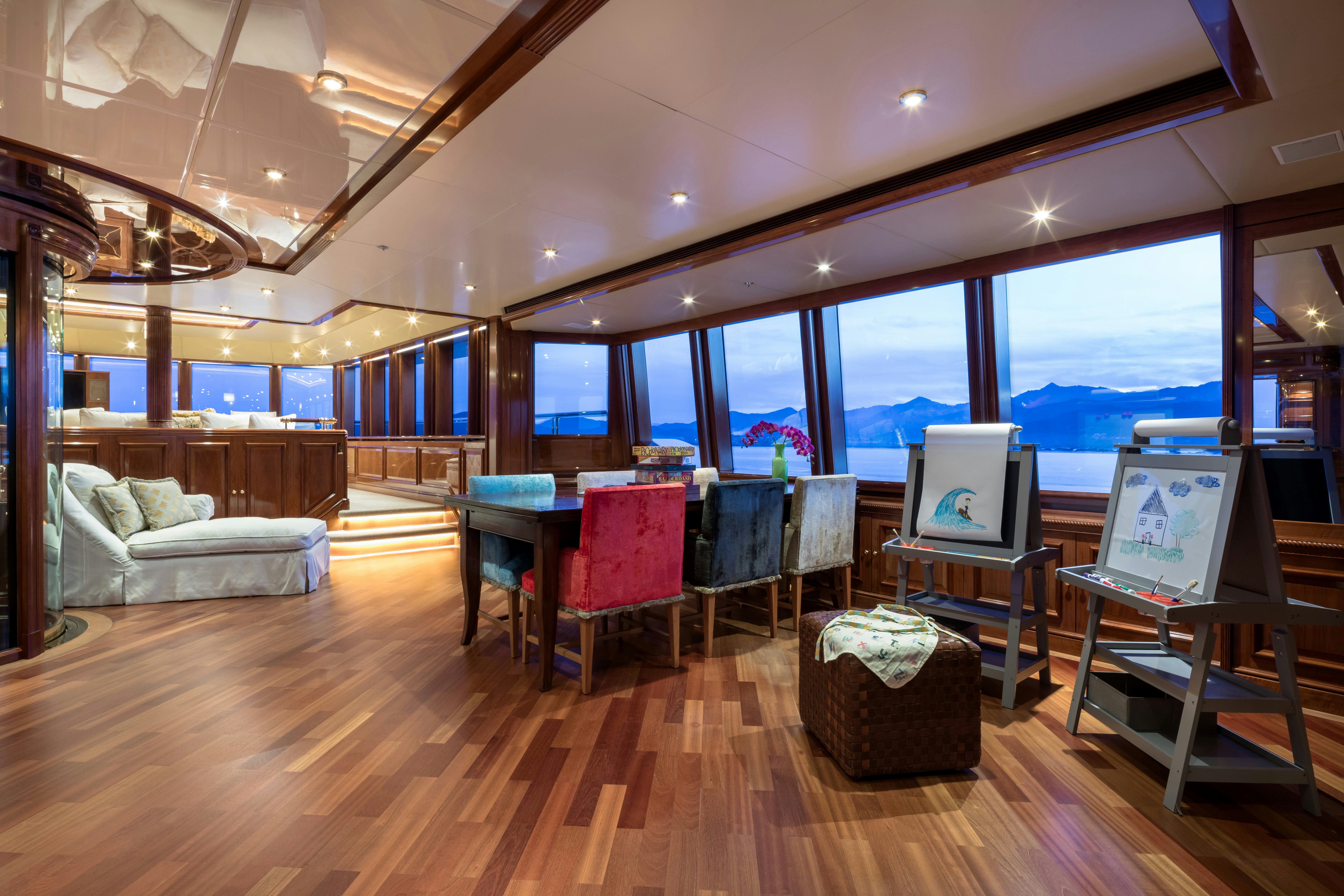 a room with a large window and a table with chairs and a television aboard STARFIRE Yacht for Charter