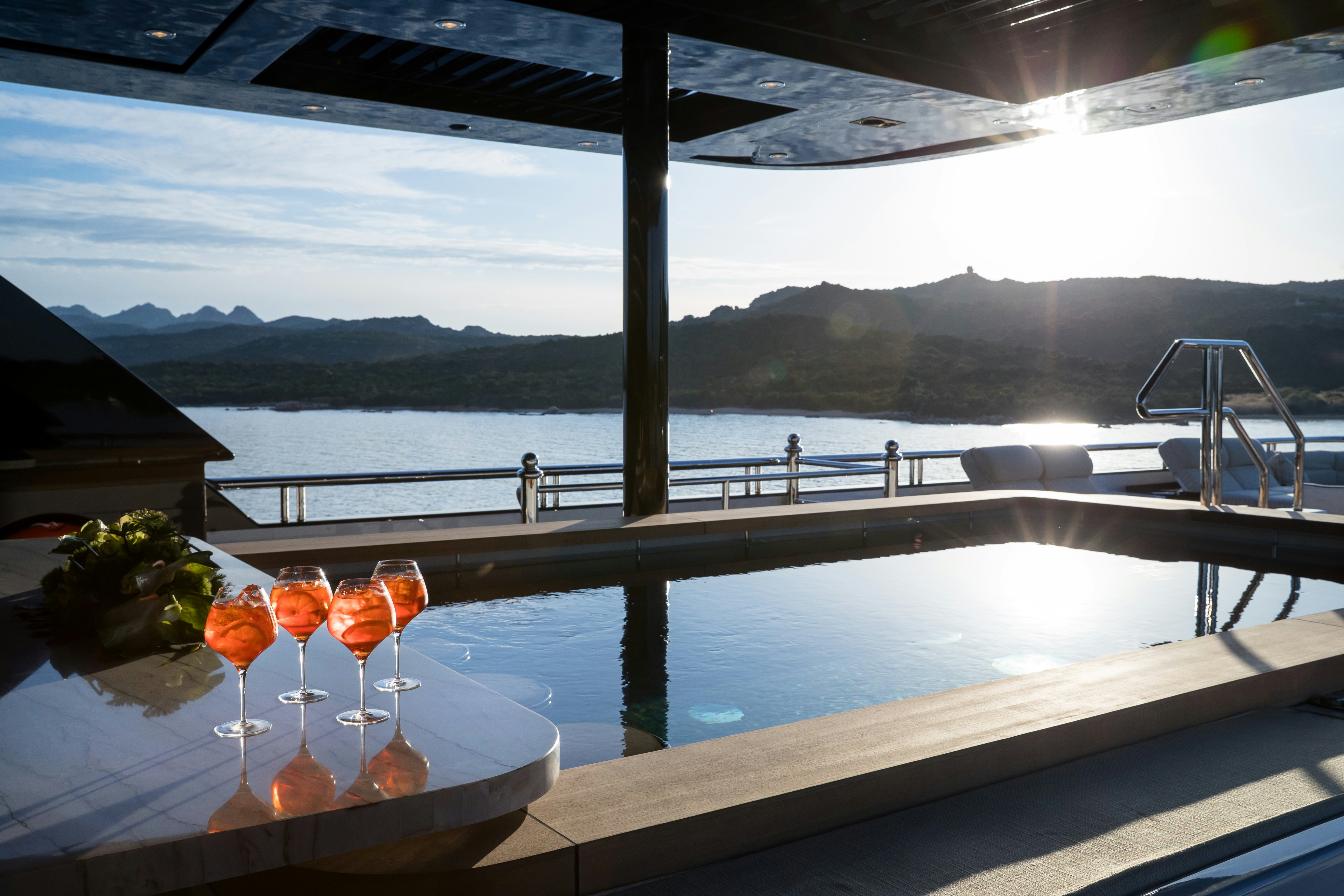 a group of glasses with orange liquid on a table by a body of water aboard STARFIRE Yacht for Charter