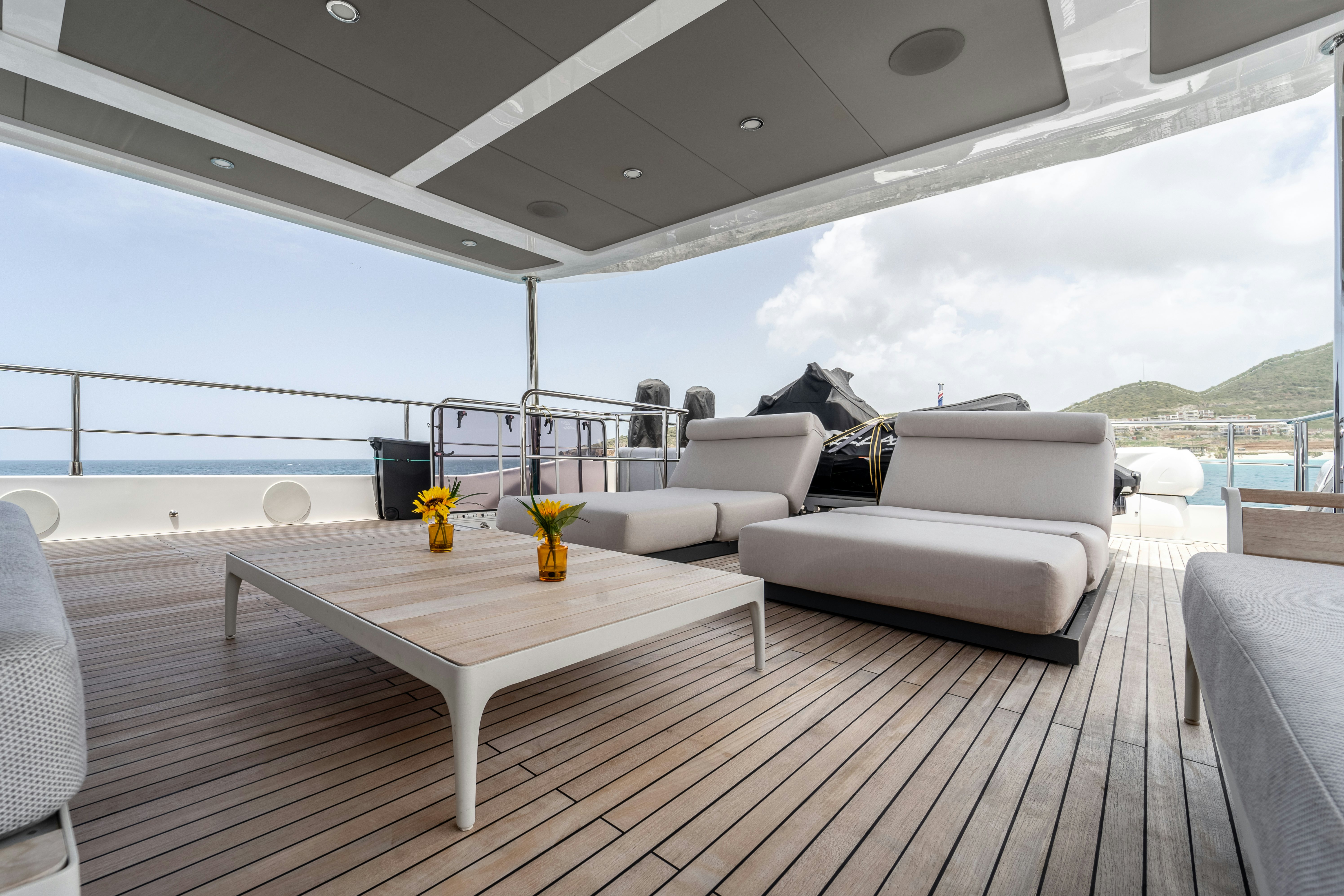 a white couch and a table on a deck with a view of the ocean and mountains aboard EXIT STRATEGY Yacht for Sale