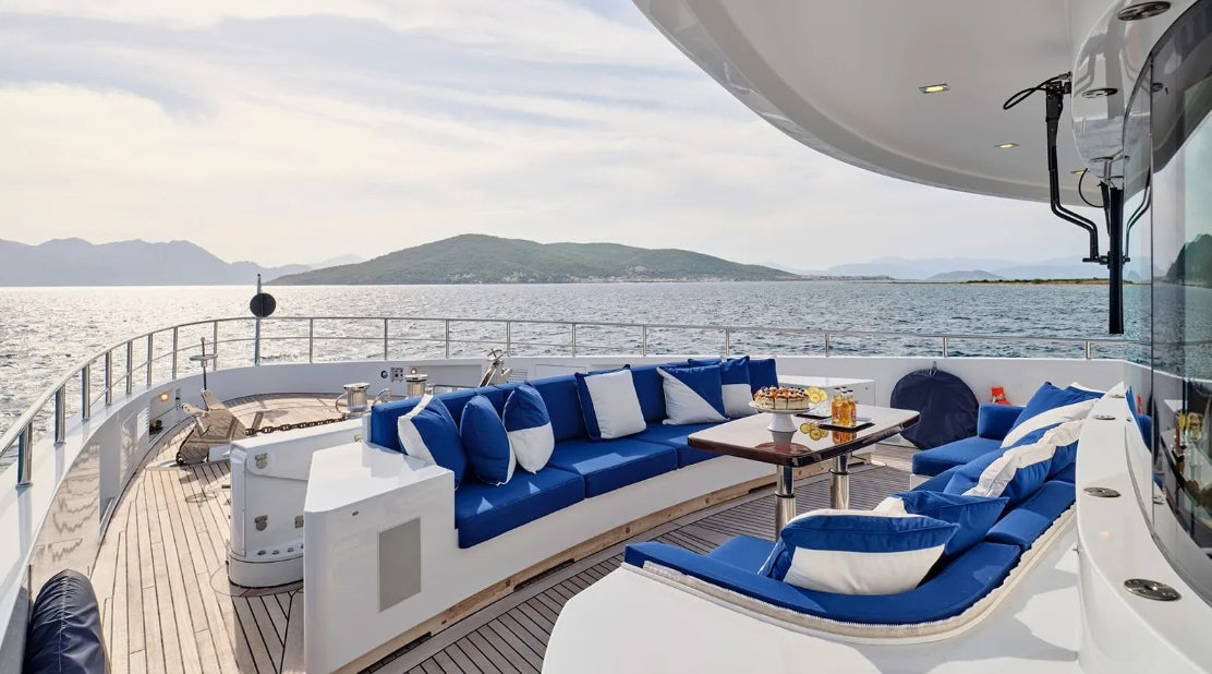a room with a bed and a table with chairs and a view of the ocean aboard TIMBUKTU Yacht for Charter