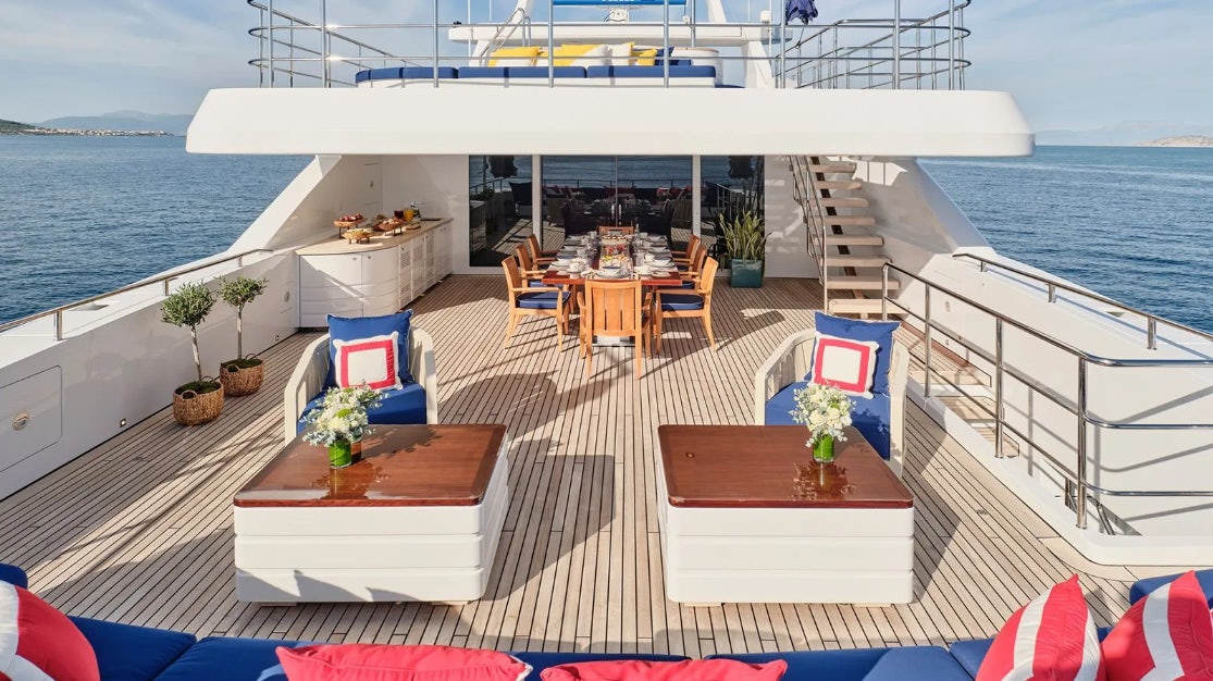 a deck with tables and chairs on it next to a body of water aboard TIMBUKTU Yacht for Charter
