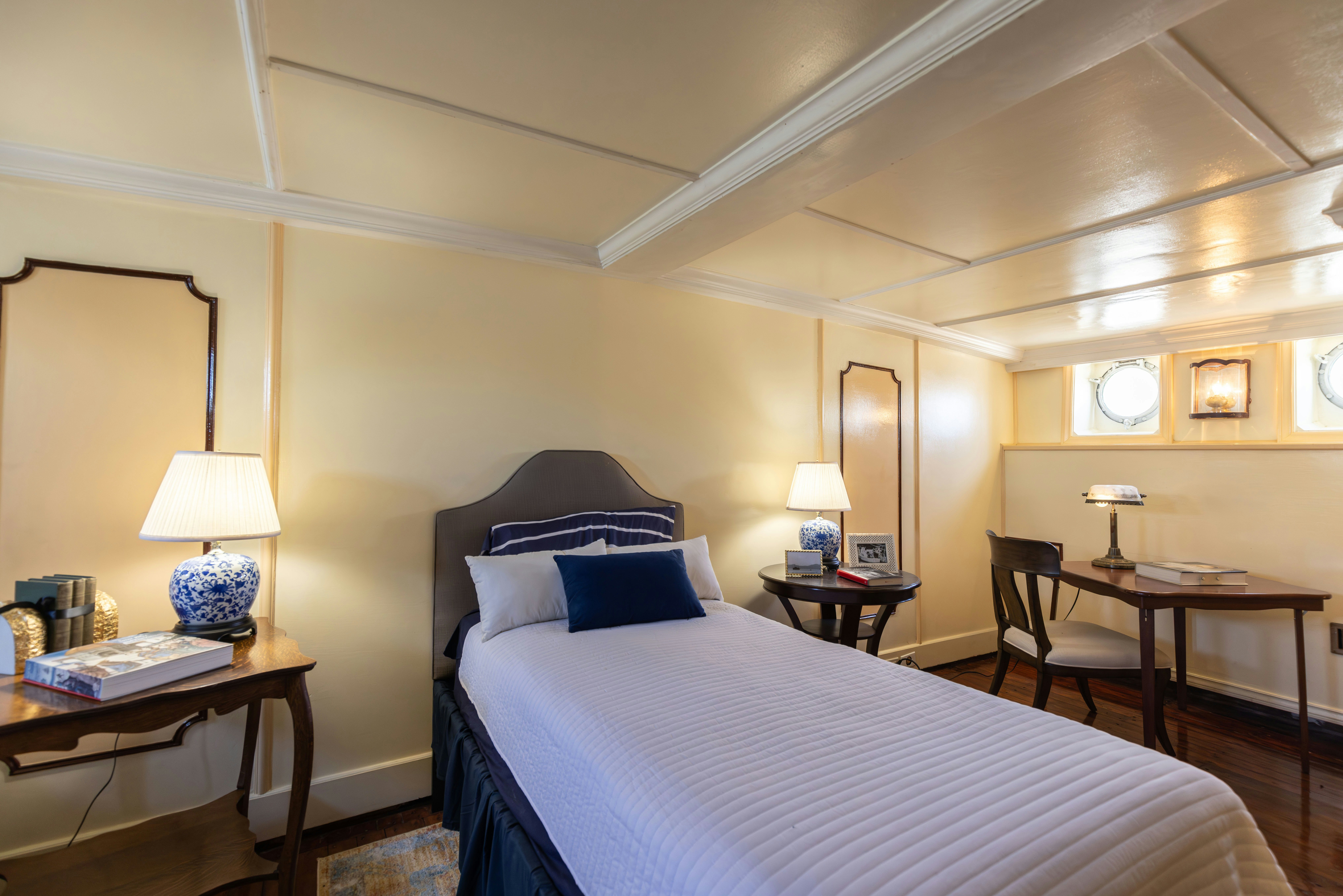 a bed with a blue and white comforter and a table with a lamp and a window with aboard NORTHWIND Yacht for Sale