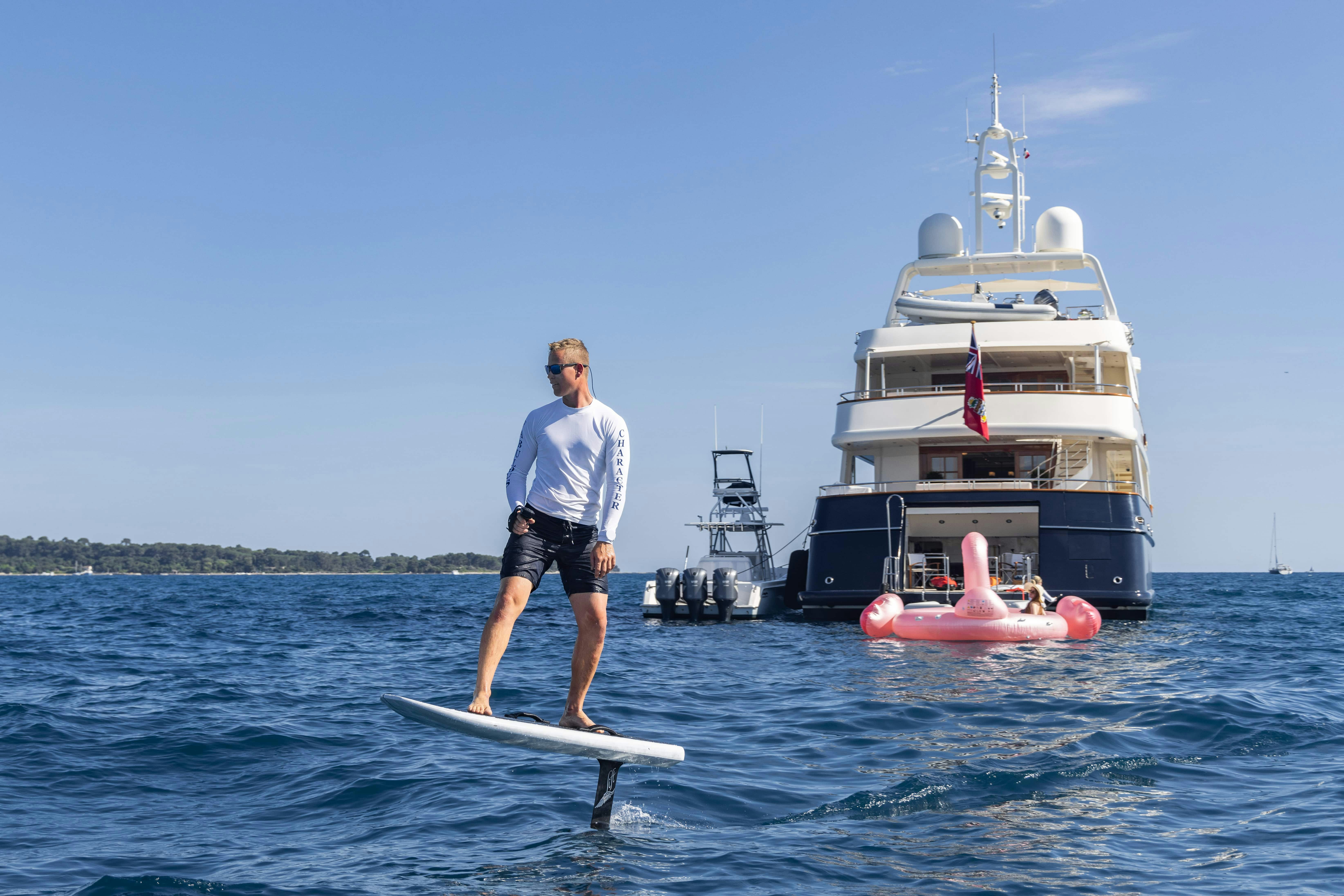 a man on a surfboard in the water next to a boat aboard FABULOUS CHARACTER Yacht for Charter
