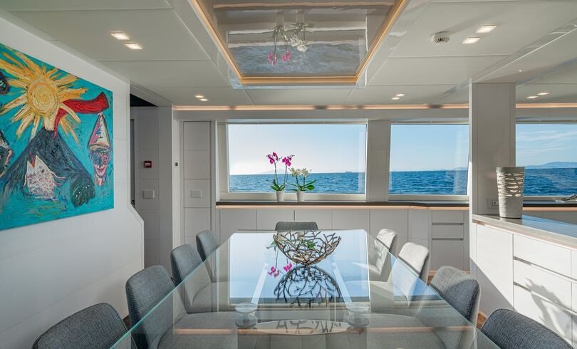 a room with a couch and a table with chairs and a window aboard SANDS Yacht for Charter