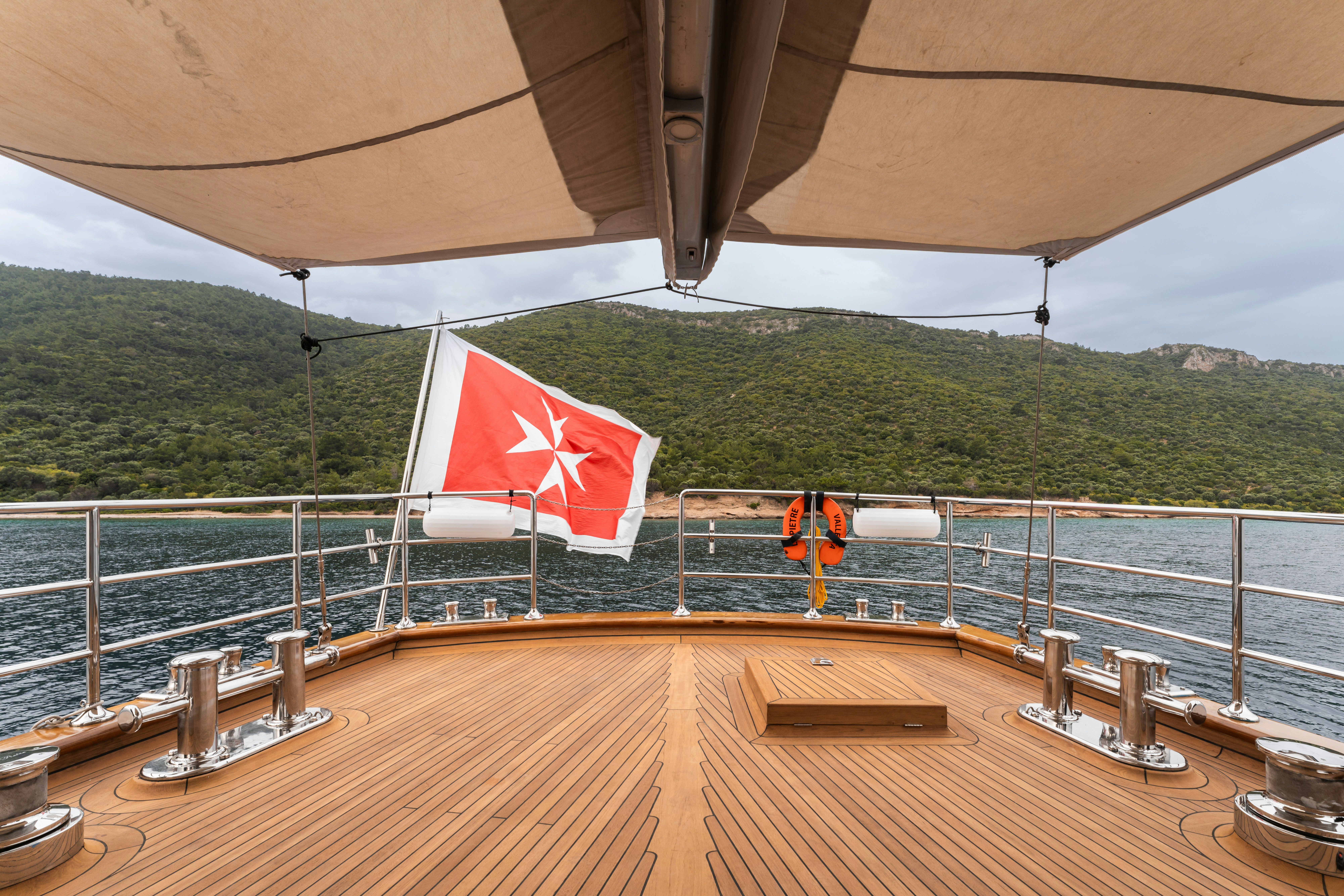 a deck with a flag and a body of water in the background aboard LE PIETRE Yacht for Sale