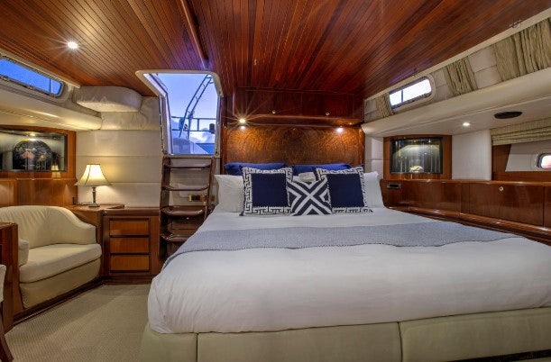 a bed with a white sheet and pillows in a room with a wood ceiling and a window with aboard SORCERER II Yacht for Sale