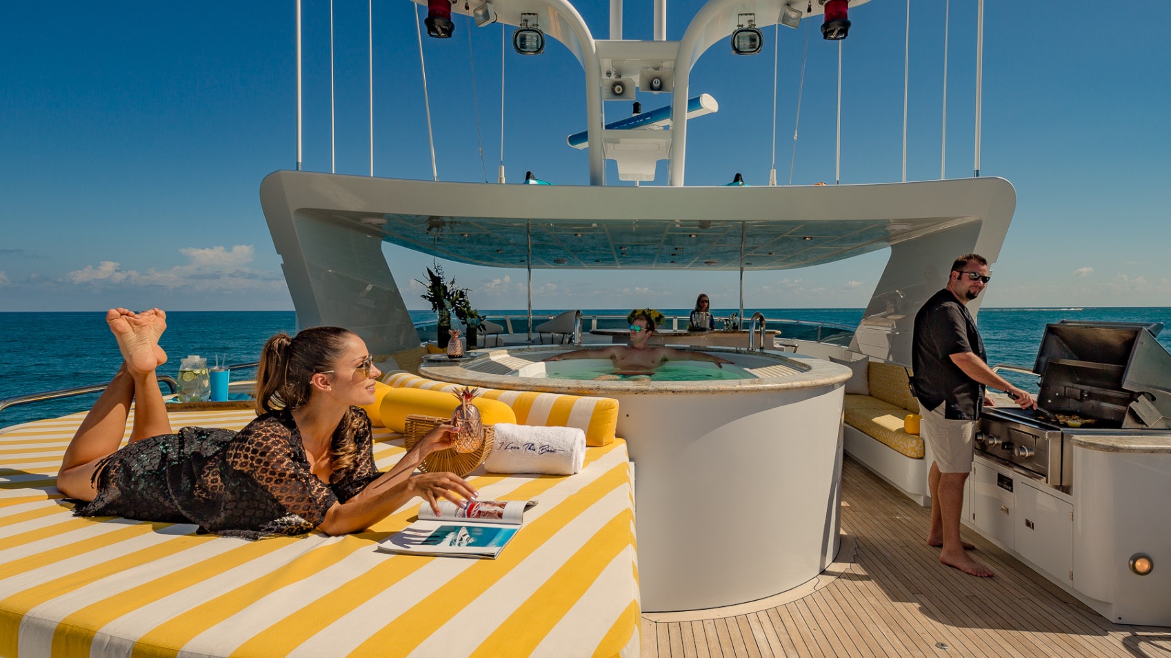 a woman sitting on a lounge chair on a deck with a man standing by her aboard I LOVE THIS BOAT Yacht for Sale