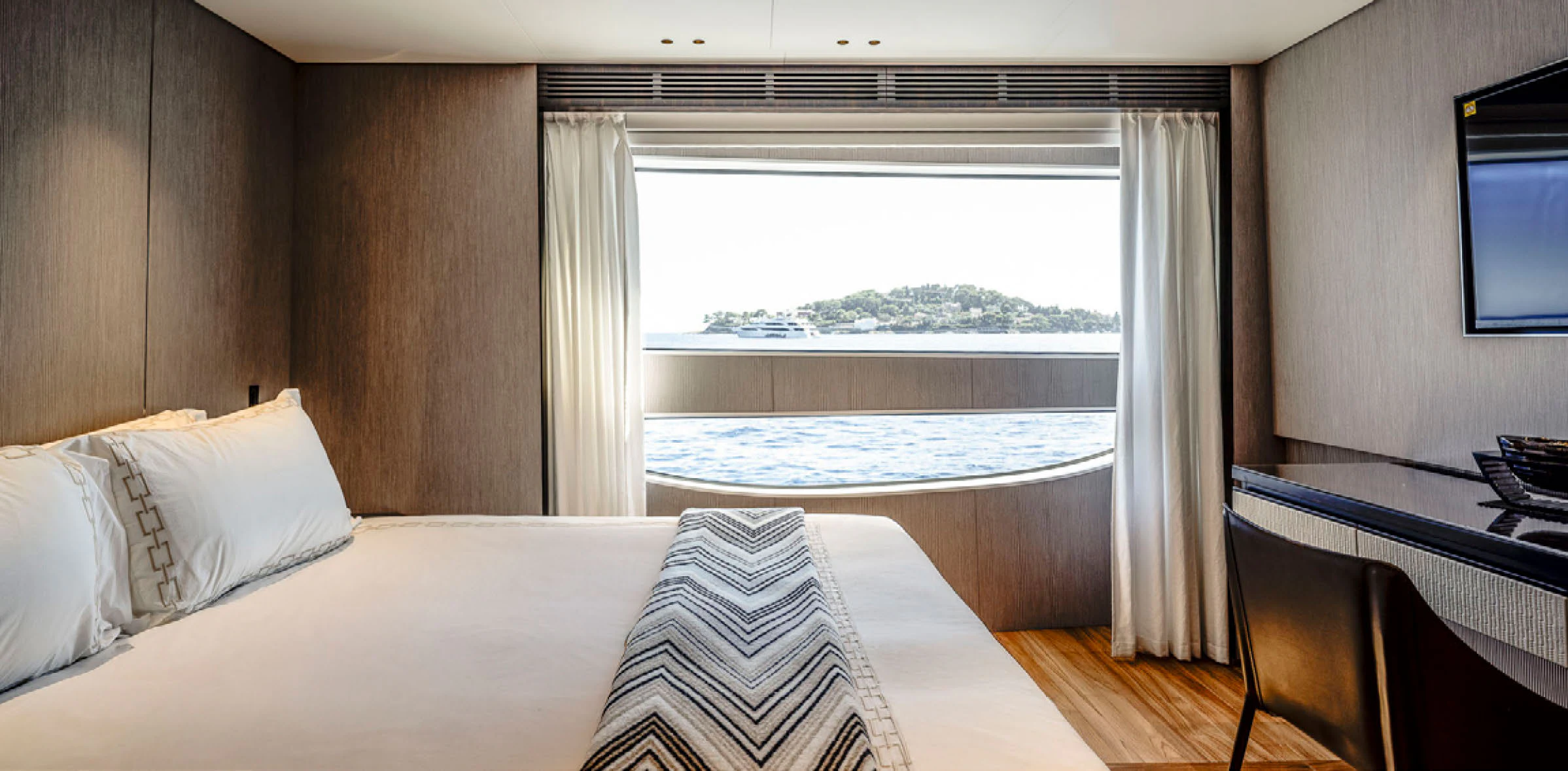 a bed with a white sheet and pillows in a room with a television aboard CADA DIA Yacht for Charter