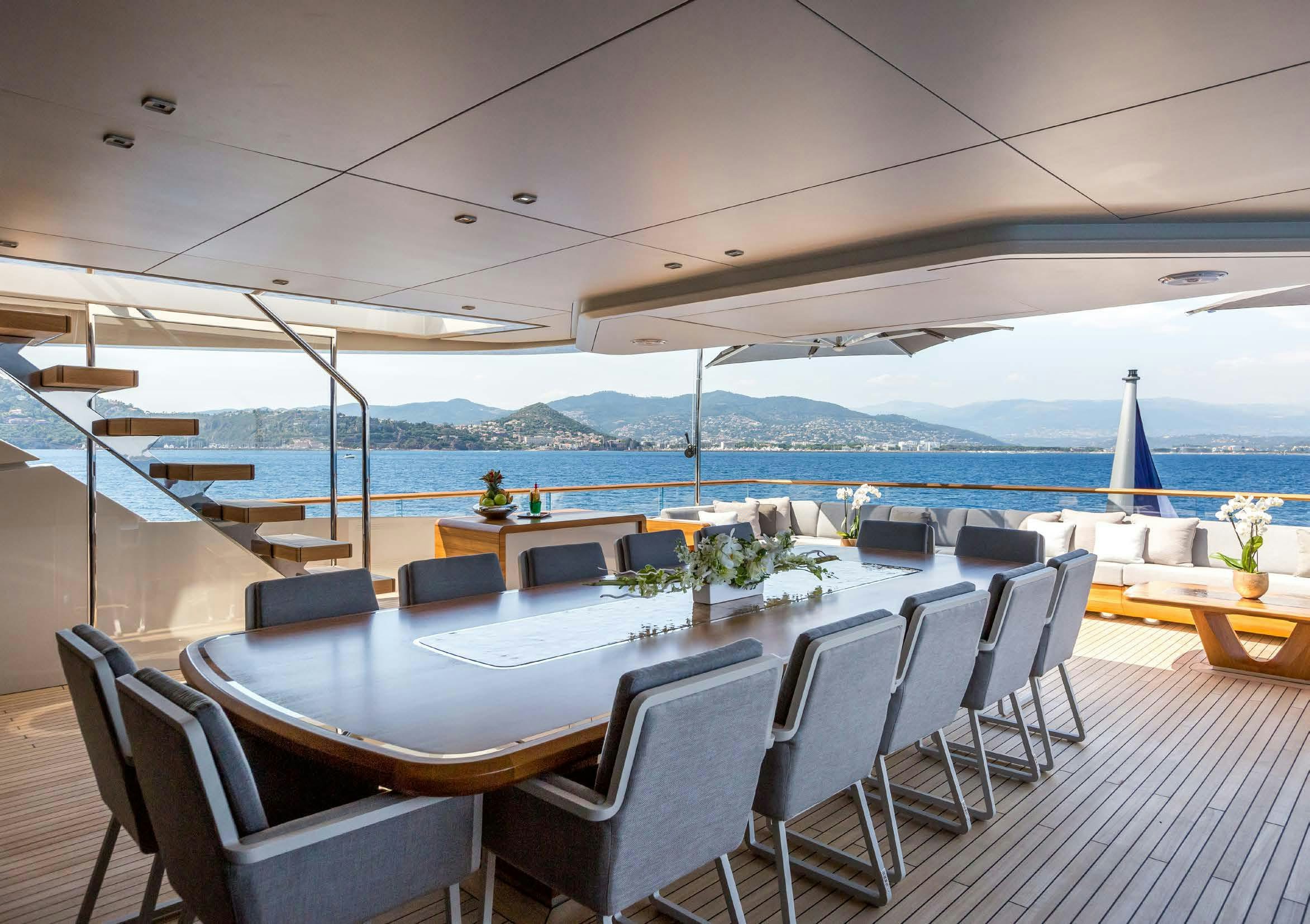 a large outdoor table with chairs and a large body of water in the background aboard VERTIGE Yacht for Sale