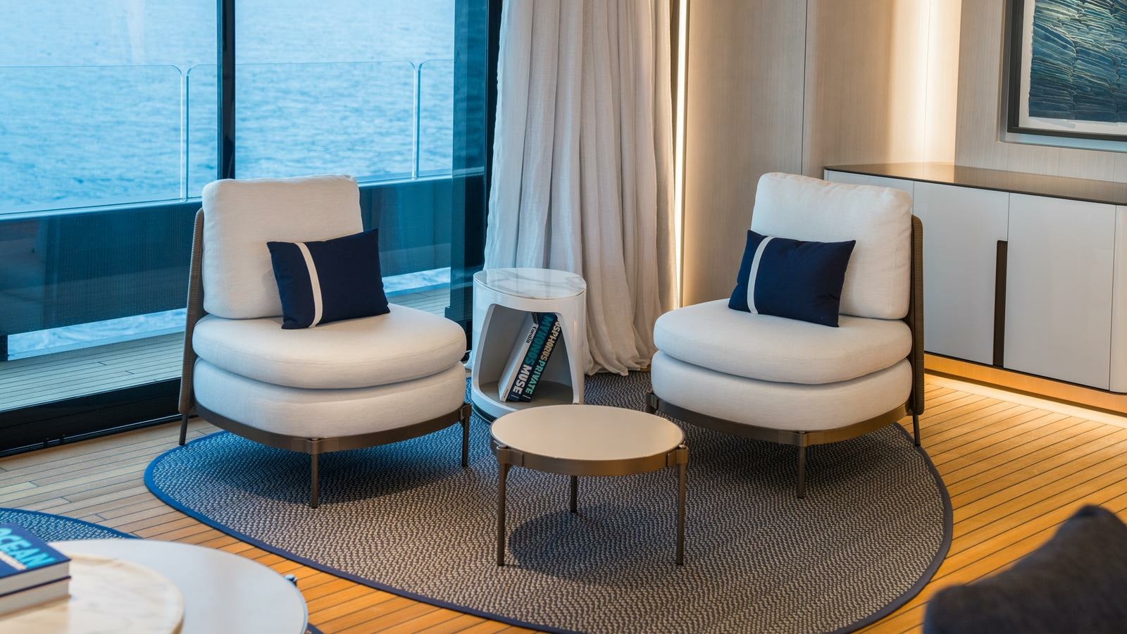 a room with a couple of chairs and a table with a book on it aboard AKULA Yacht for Charter