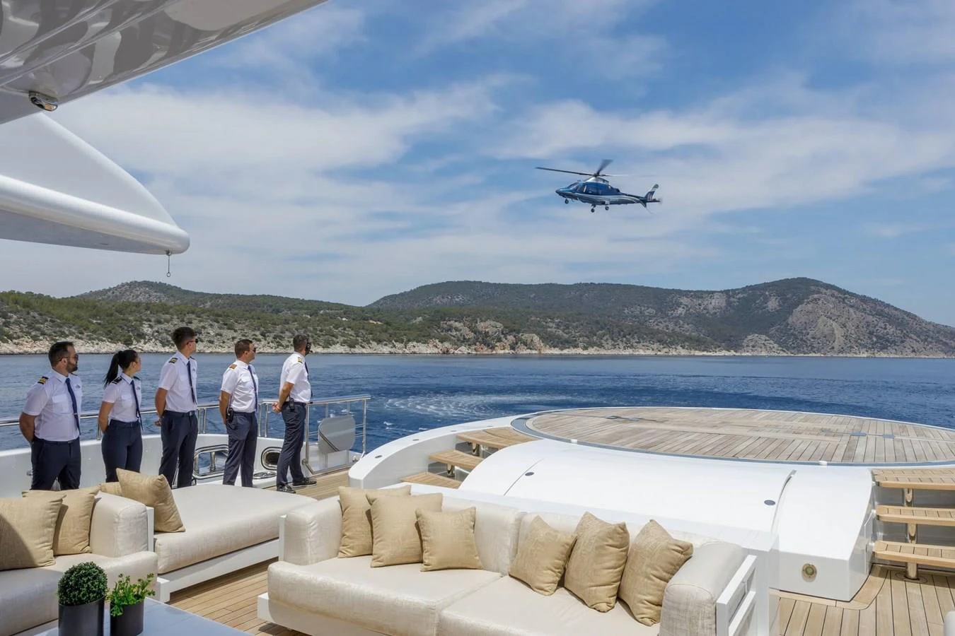 a group of people standing on a balcony looking at a helicopter flying over a body of water aboard SAPPHIRE Yacht for Charter