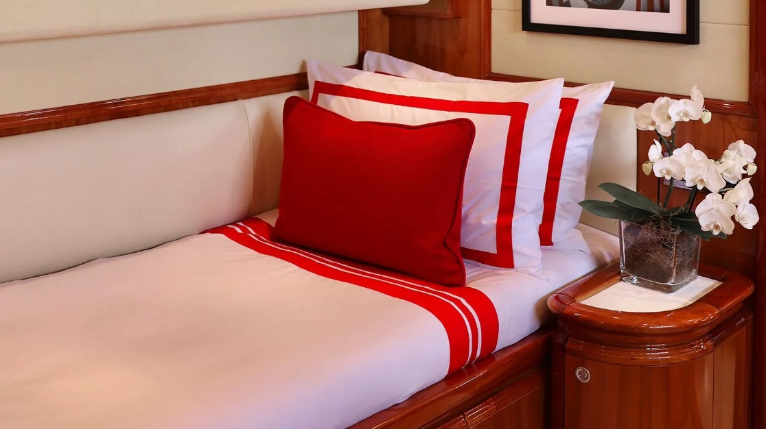 a bed with a red and white pillow and white flowers aboard CHAMPAGNE & CAVIAR Yacht for Charter
