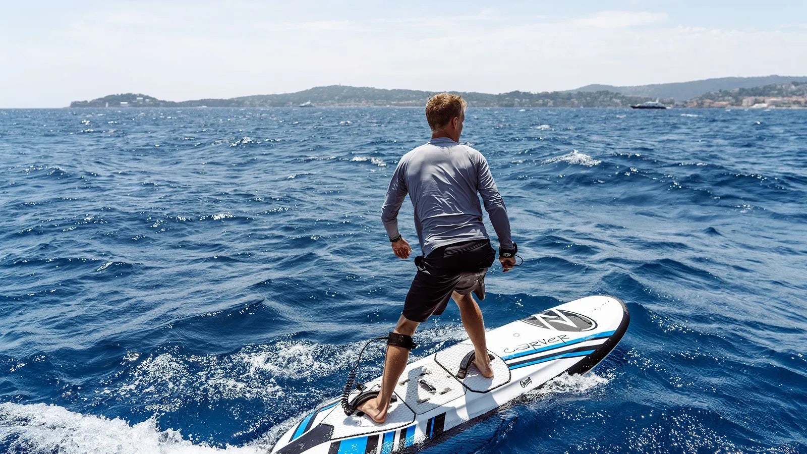 a man standing on a surfboard in the ocean aboard AWAY Yacht for Charter