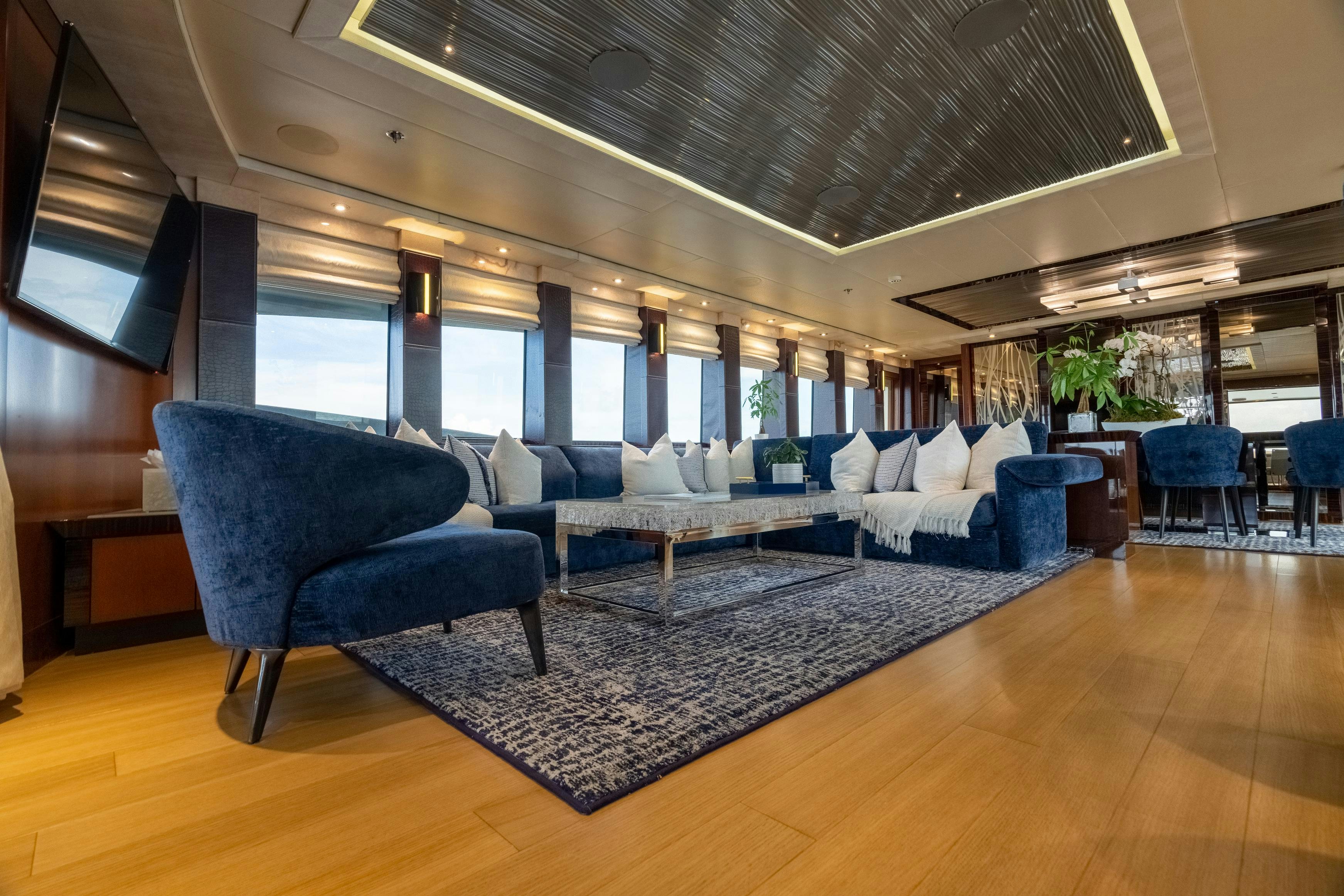 a large living room with a large blue chair and a large window aboard AQUANOVA Yacht for Charter