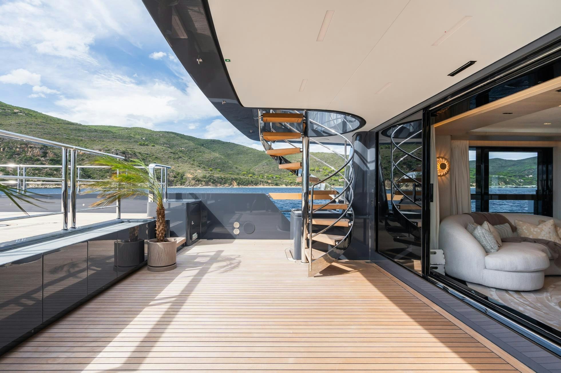 a deck with a large glass door and a railing with a view of a mountain range and a aboard M Yacht for Sale