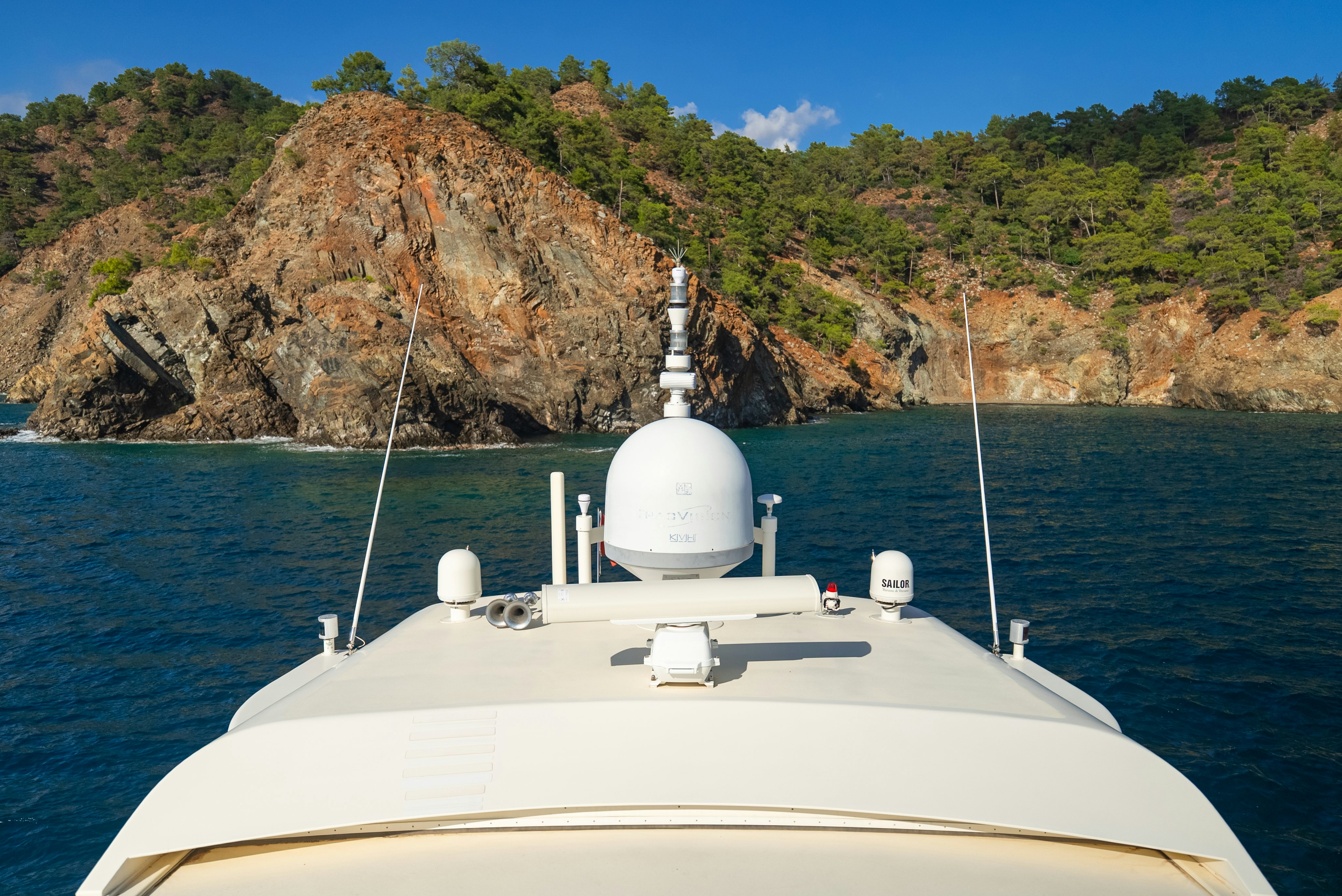 a white boat with a white tower on the water by a rocky cliff aboard CLARITA Yacht for Sale