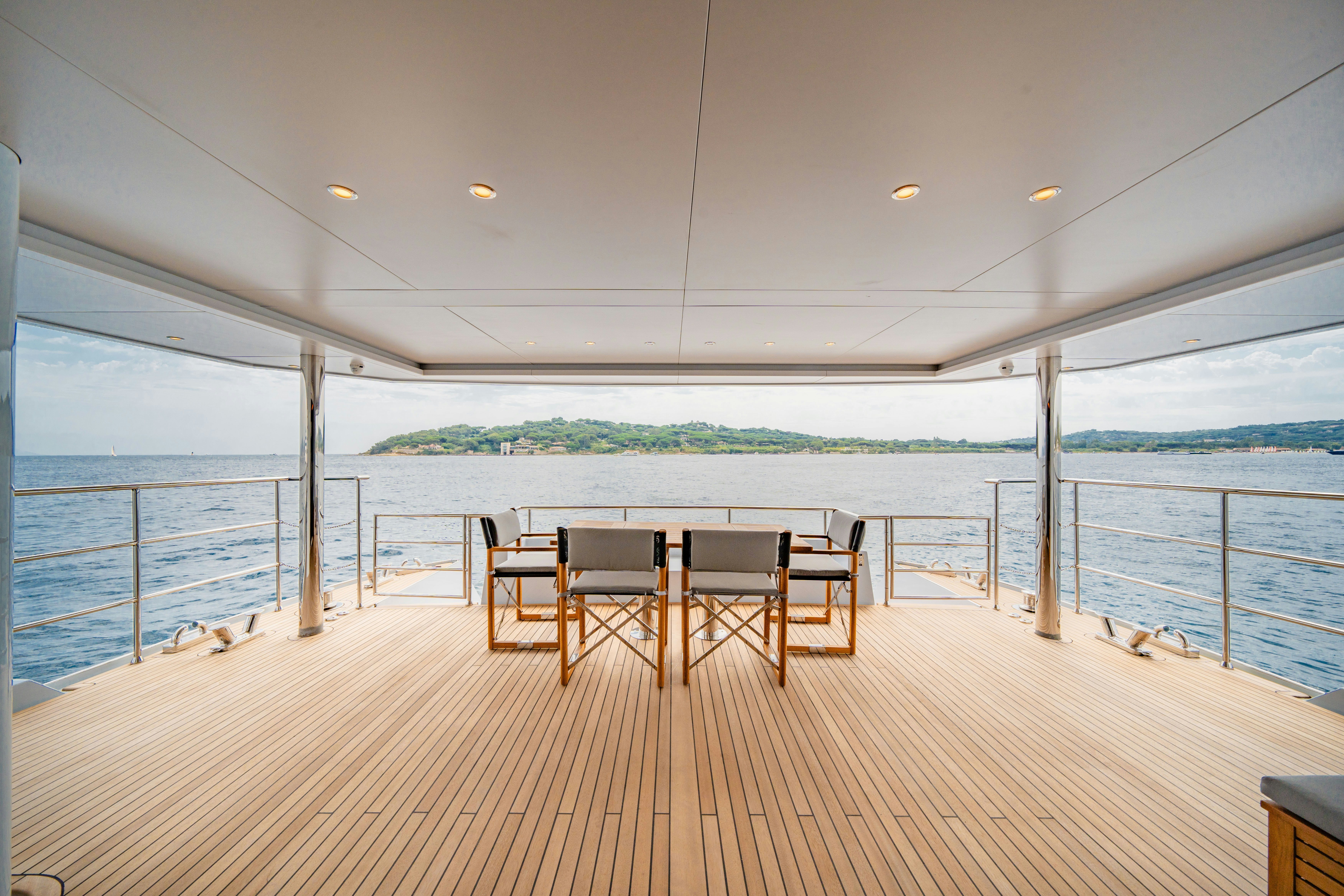 a wooden deck with chairs and a body of water in the background aboard ICE Yacht for Sale