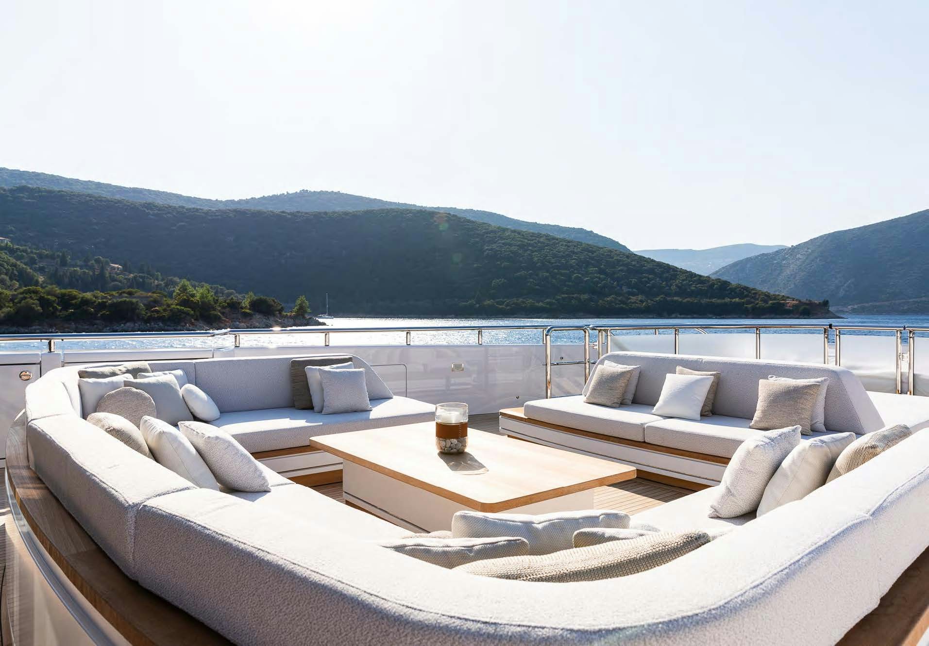 a large white couch with a glass of beer on a balcony overlooking a large body of water and aboard ALUNYA Yacht for Charter