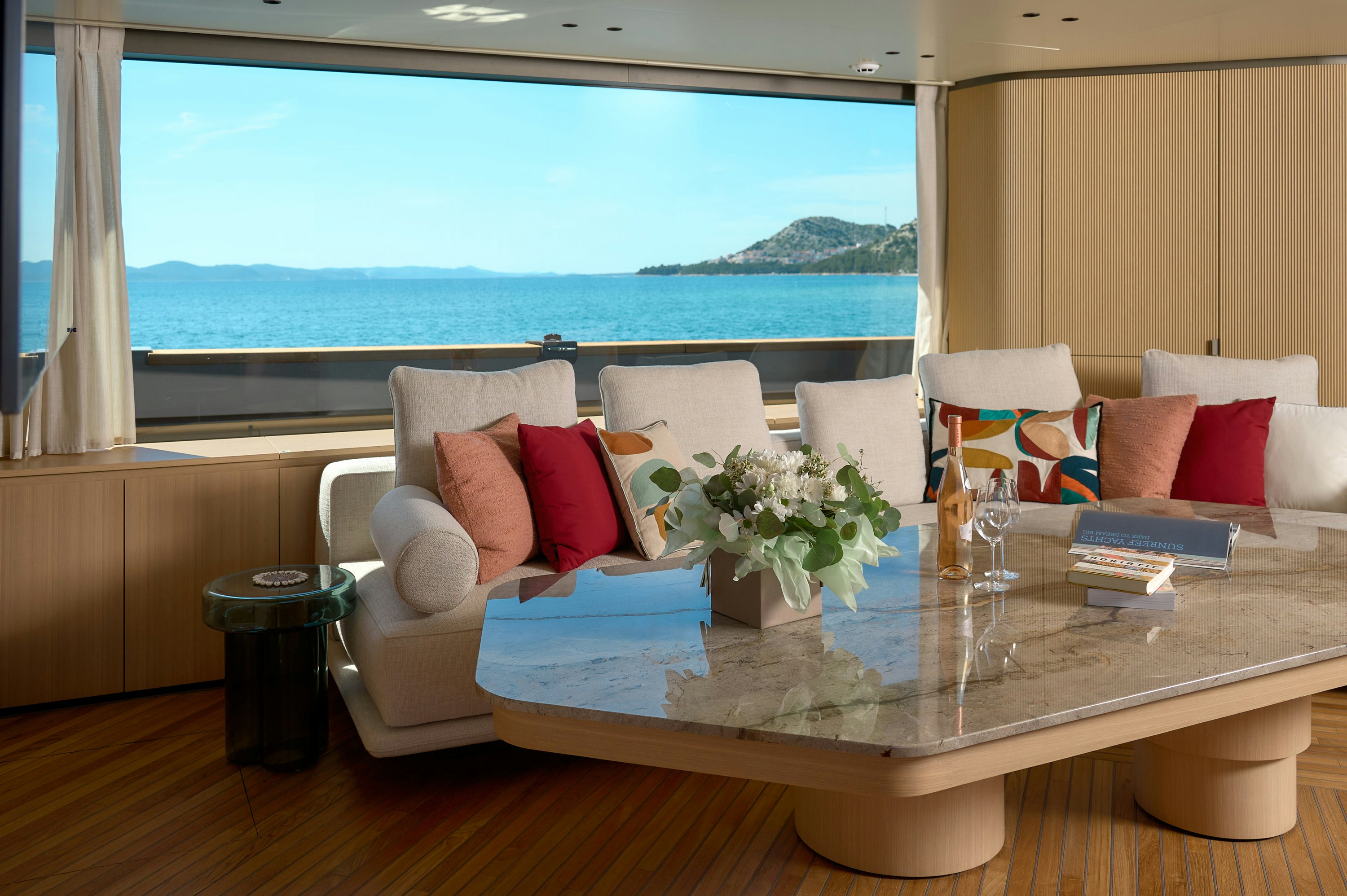 a table with pillows and a glass window with a view of the ocean aboard AZZURRI Yacht for Charter