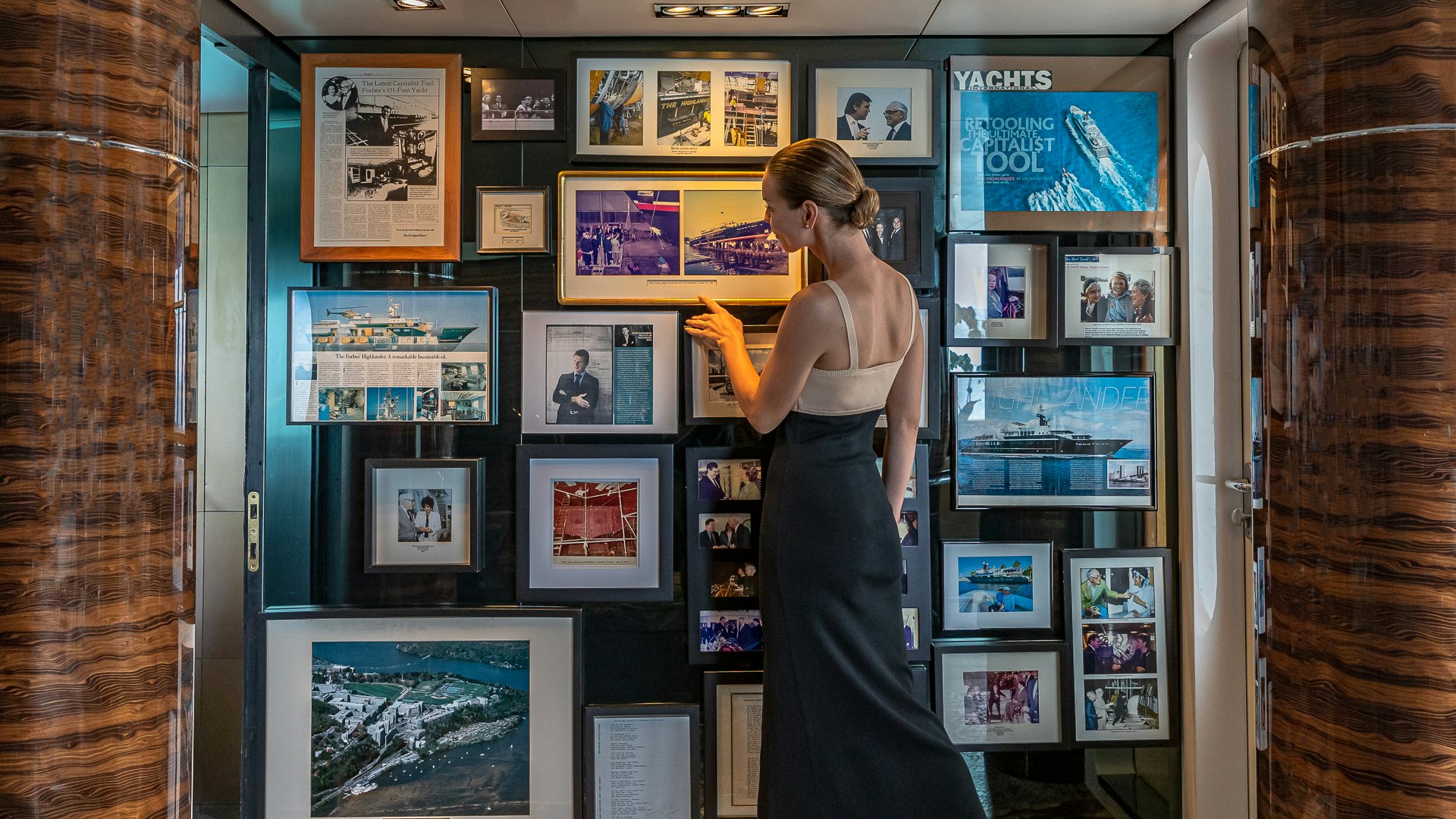 a person in a black dress holding a pair of scissors in front of a display of pictures aboard HIGHLANDER Yacht for Charter
