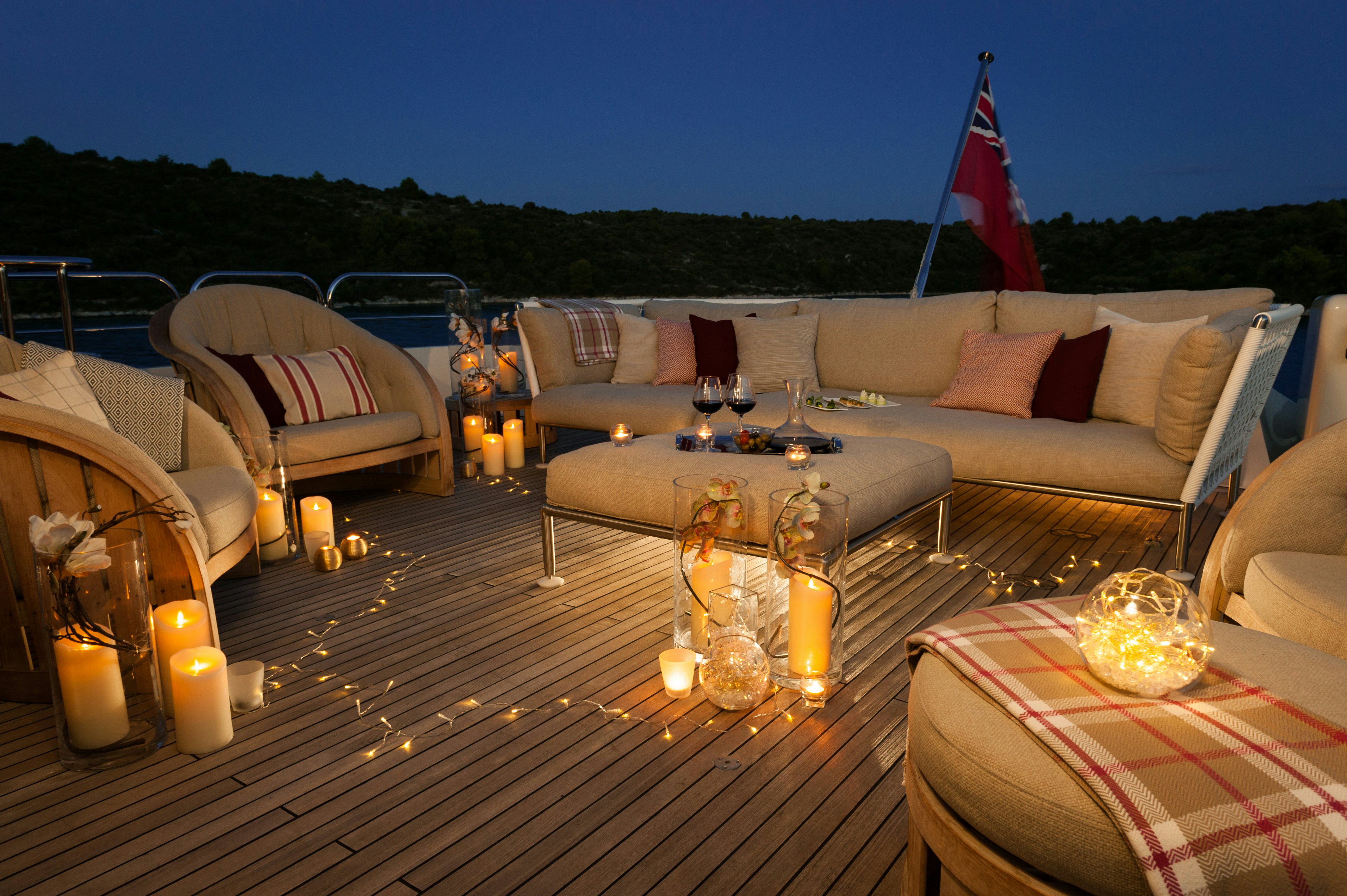 a table with candles and a flag on a deck with a view of a field and blue sky aboard METSUYAN IV Yacht for Charter