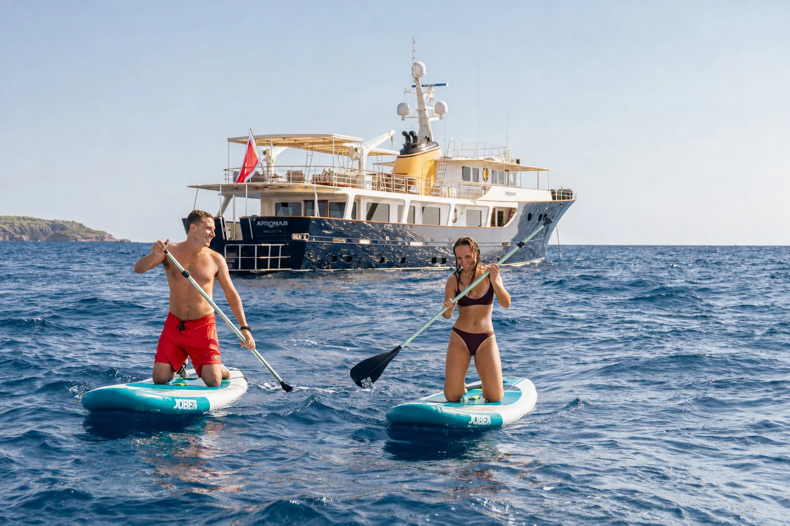 a woman and a man on a paddle board in the water aboard ARIONAS Yacht for Charter