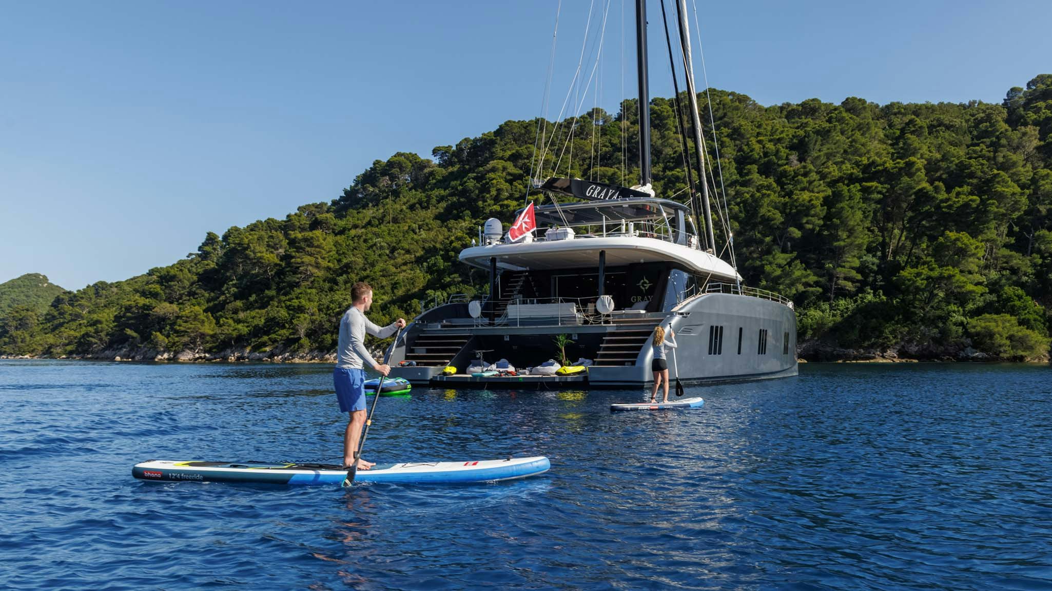 a man on a surfboard next to a sailboat aboard GRAYA Yacht for Charter