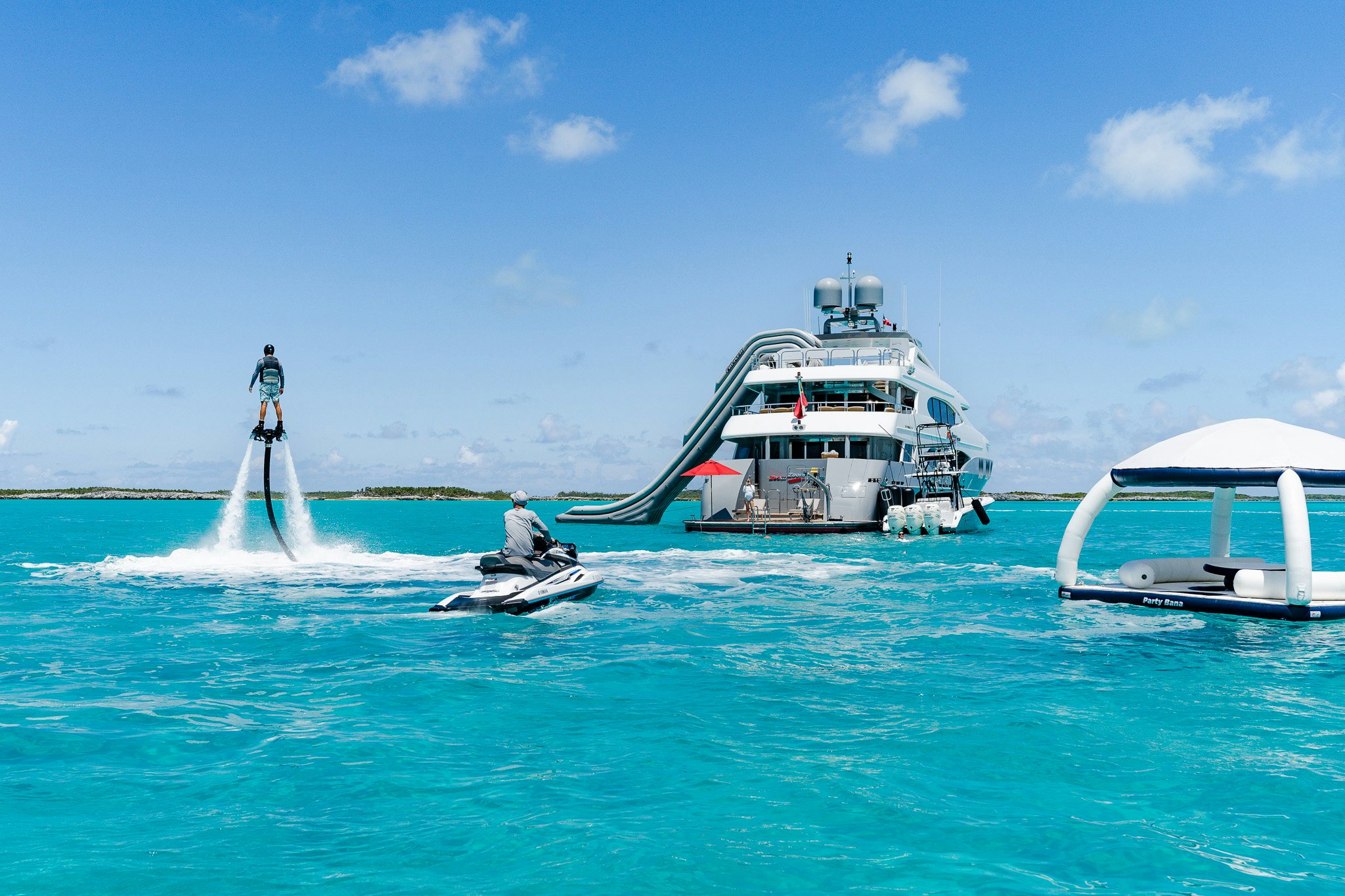 a man on a jet ski in the ocean next to a boat aboard ZOOM ZOOM ZOOM Yacht for Charter