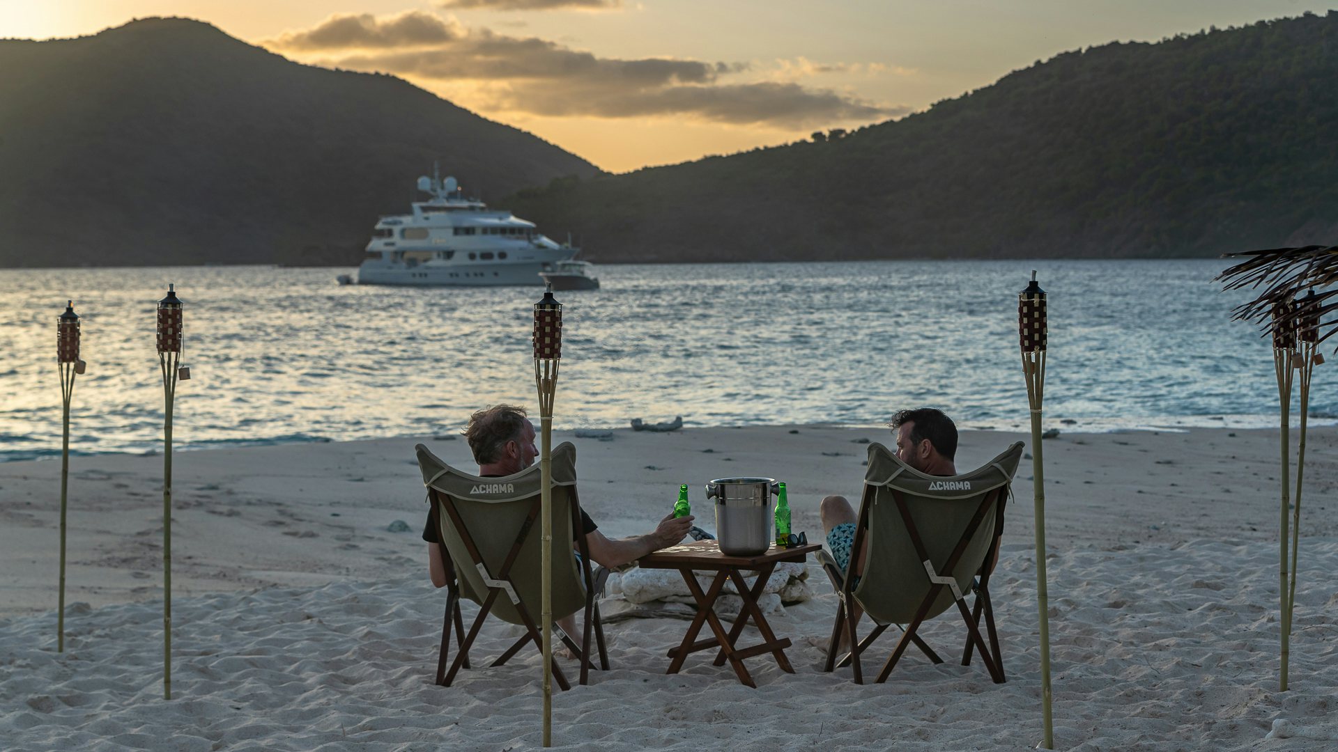 a person and a child sitting at a table on a beach with a ship in the background aboard MILESTONE Yacht for Charter