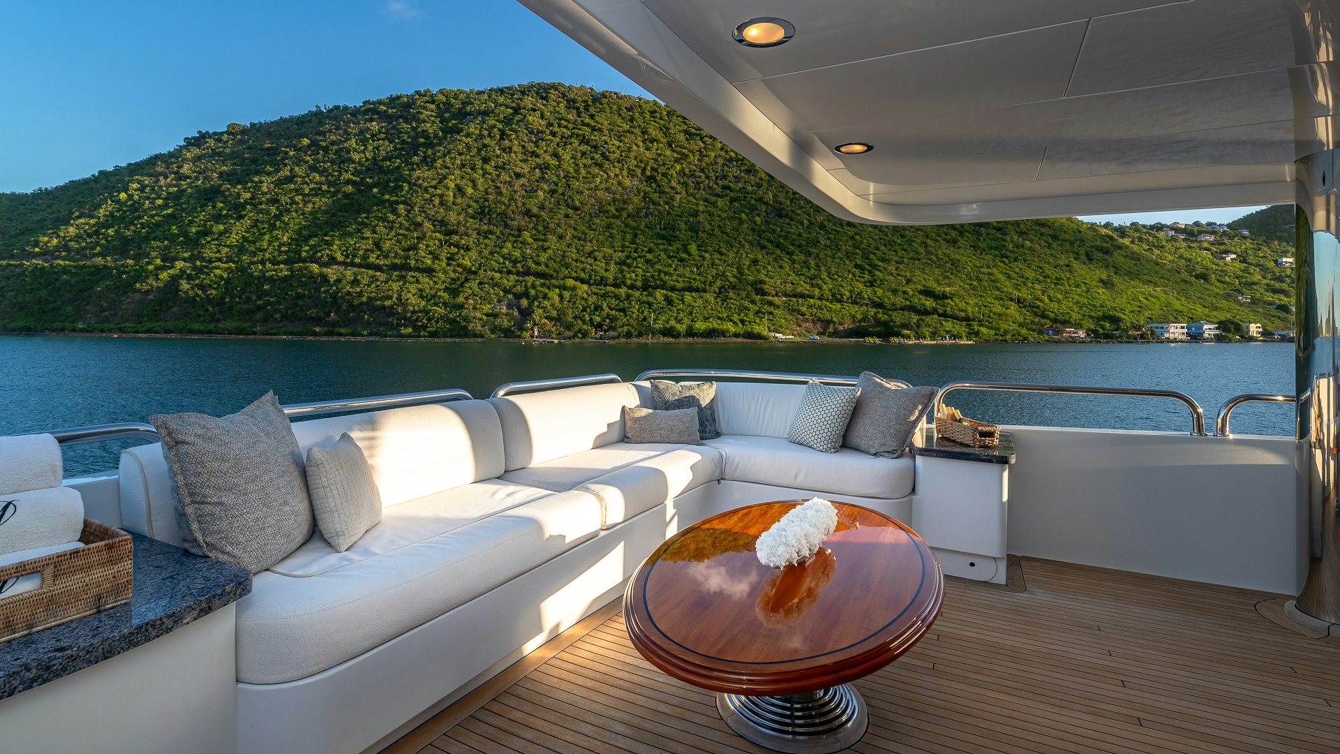 a large white couch with a round table on a wooden deck overlooking a large body of water aboard MILESTONE Yacht for Charter