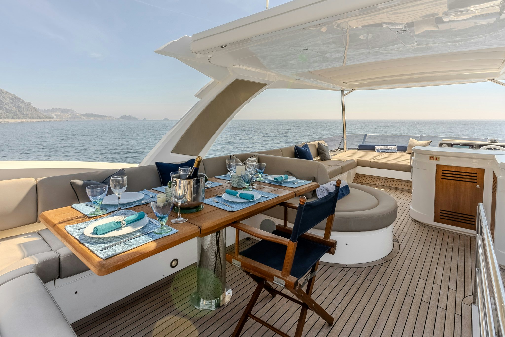 a table with chairs and a couch on a deck with water and mountains in the background aboard ISLA DE FLORA Yacht for Sale