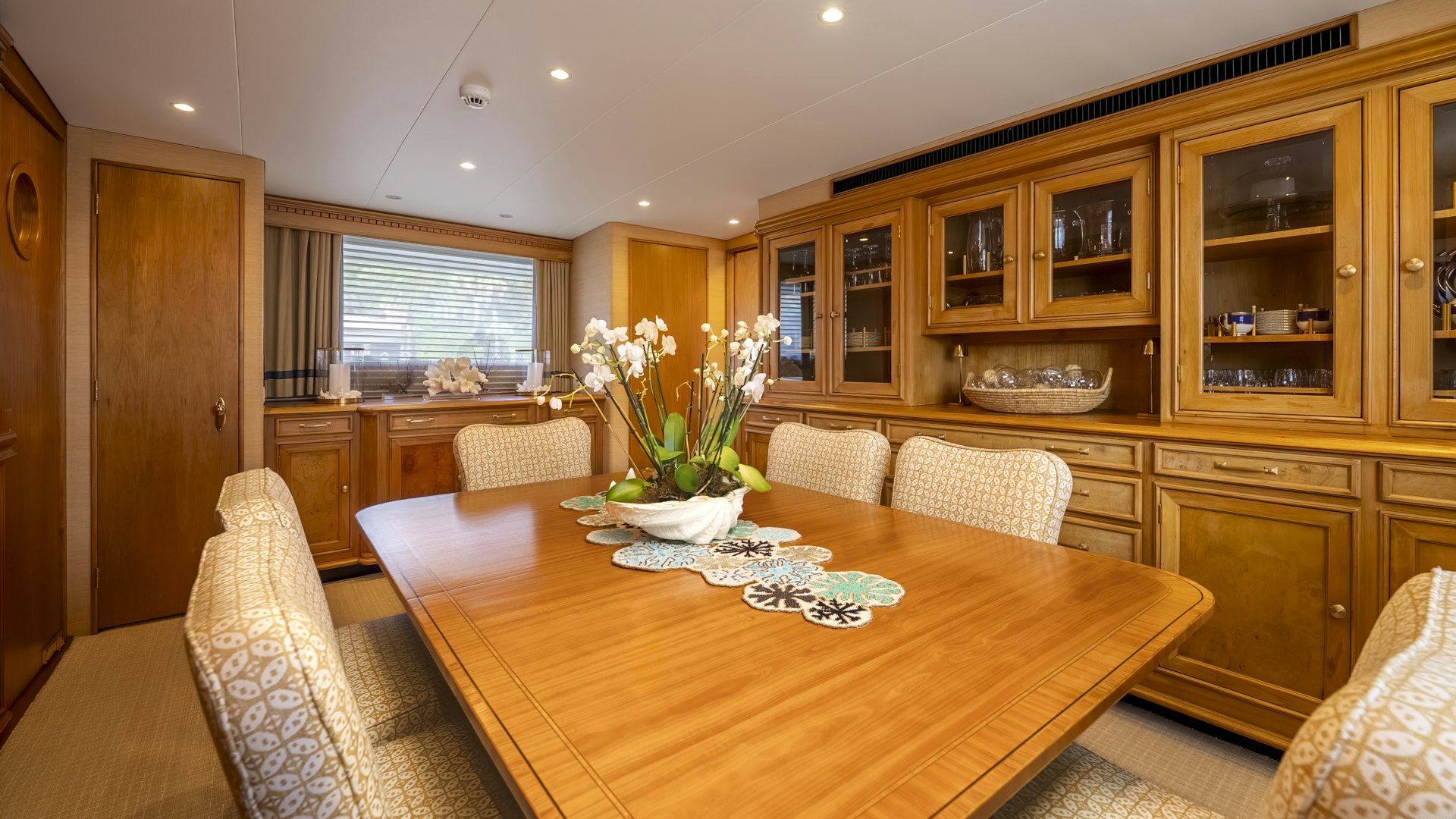 a dining table with chairs and a couch in a room with wood cabinets aboard STONEFACE Yacht for Sale