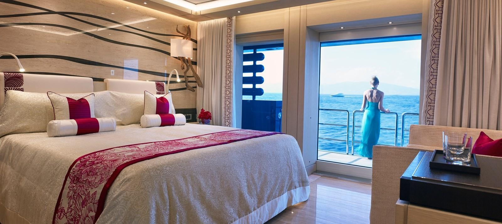 a bed with a pink bedspread and a window with a view of the ocean aboard DRAAK Yacht for Sale