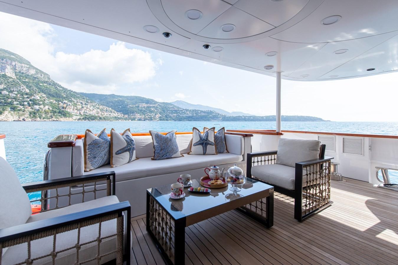 a large white couch and a table on a deck overlooking a body of water aboard BINA Yacht for Sale