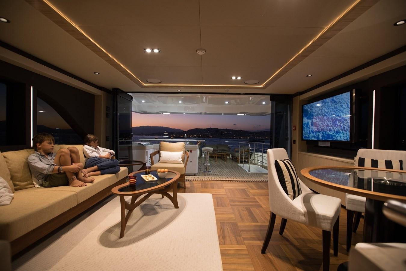 a person sitting on a couch in a living room with a large screen aboard LEGACY Yacht for Sale