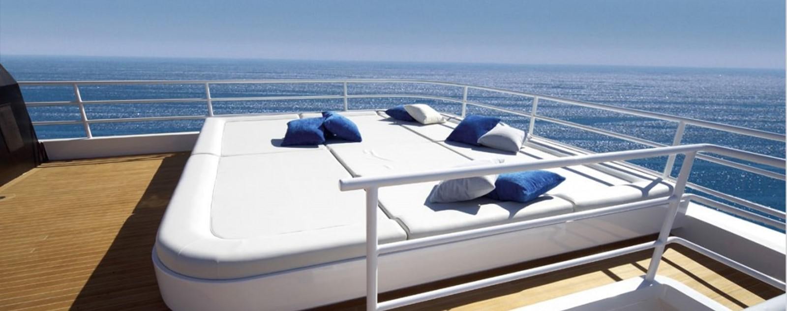 a white boat with blue pillows on a deck with a blue hat on it aboard OCEAN KING 88 Yacht for Sale