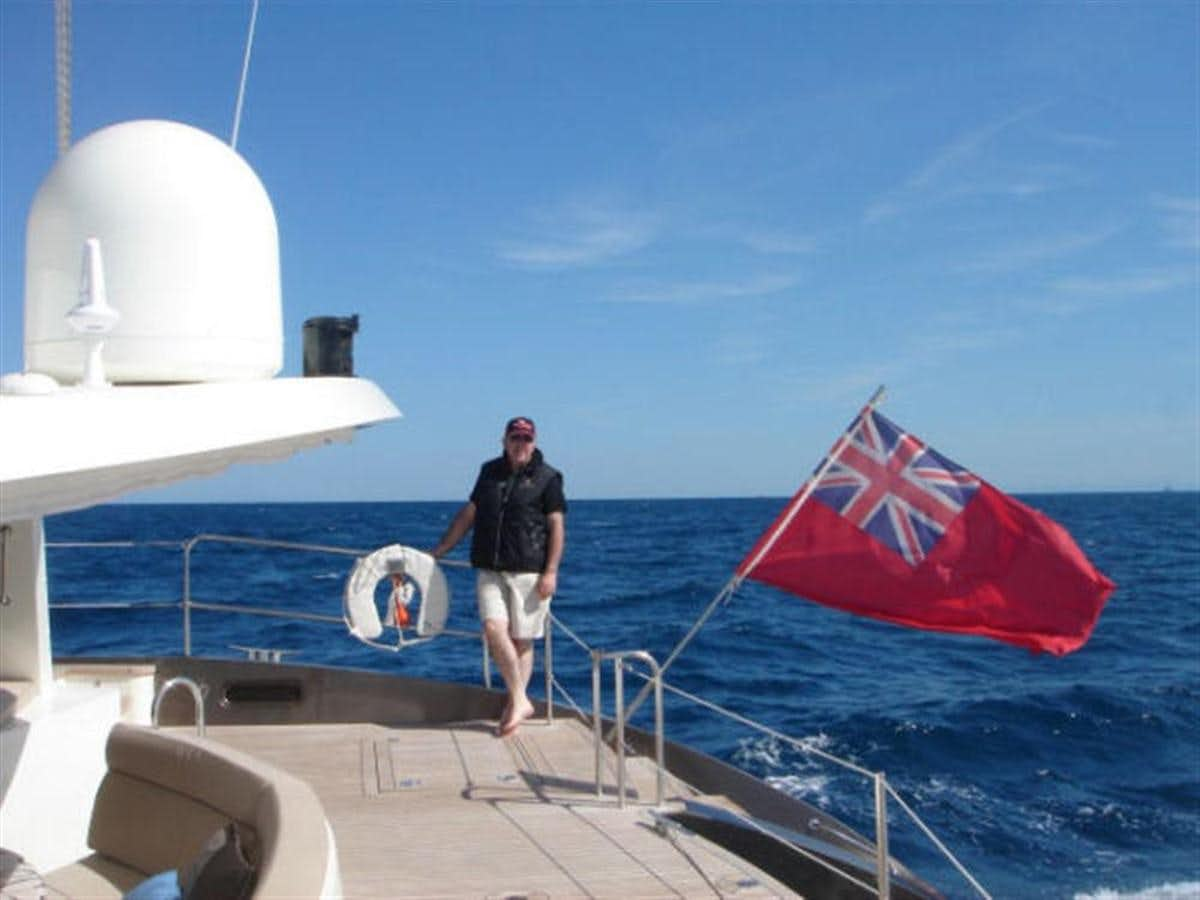 a person standing on a boat with a flag on the front aboard 75' 2008 YAPLUKA LUXURY CATAMARAN Yacht for Sale