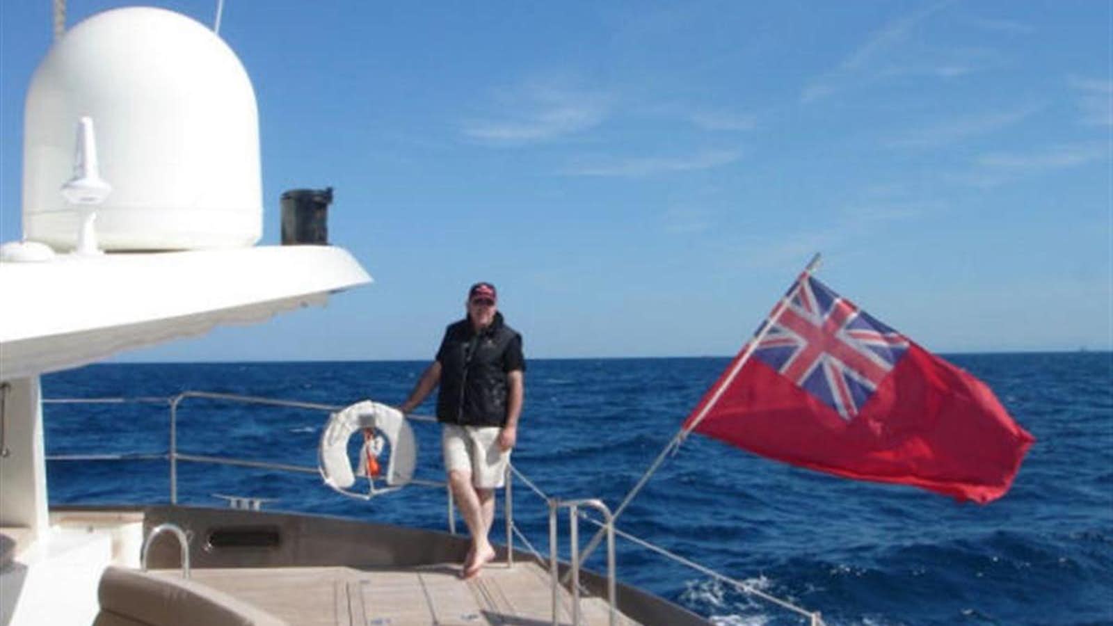 a person standing on a boat with a flag on the front aboard 75' 2008 YAPLUKA LUXURY CATAMARAN Yacht for Sale
