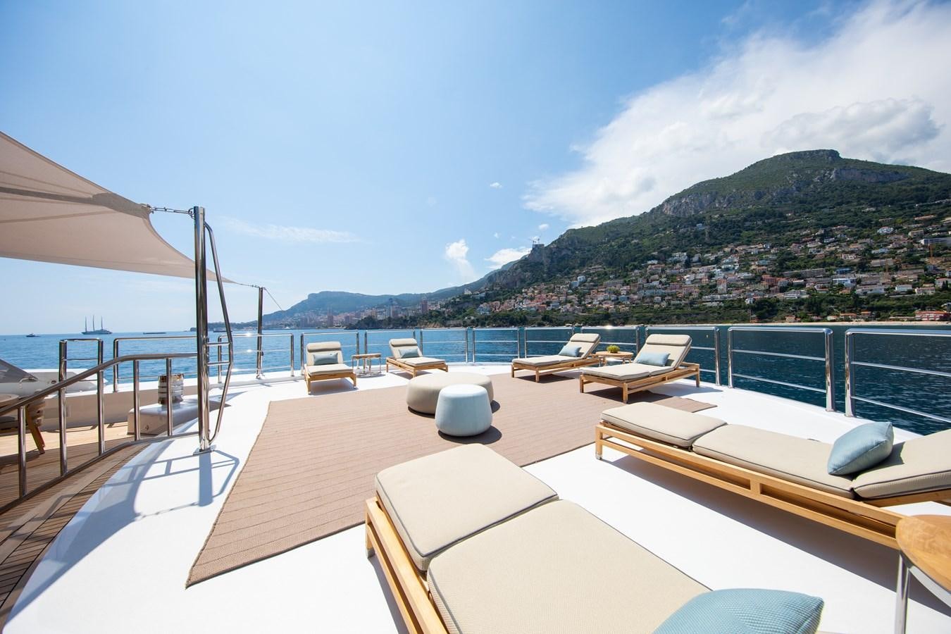 a deck with lounge chairs on it and a body of water in the background aboard AHS Yacht for Sale