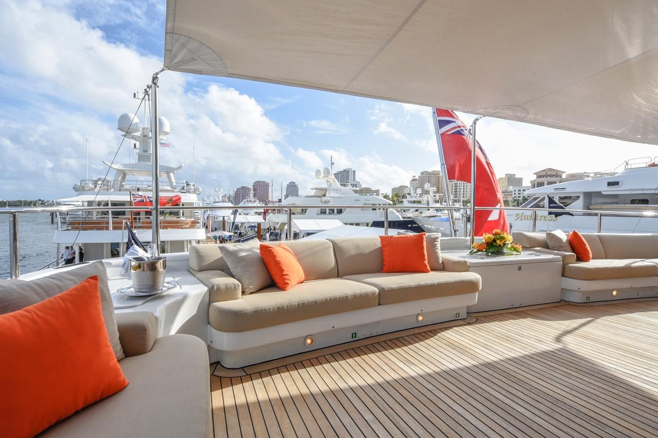 a large white lounge chair with a red and white pillow on a deck overlooking a large city with aboard TE MANU Yacht for Sale