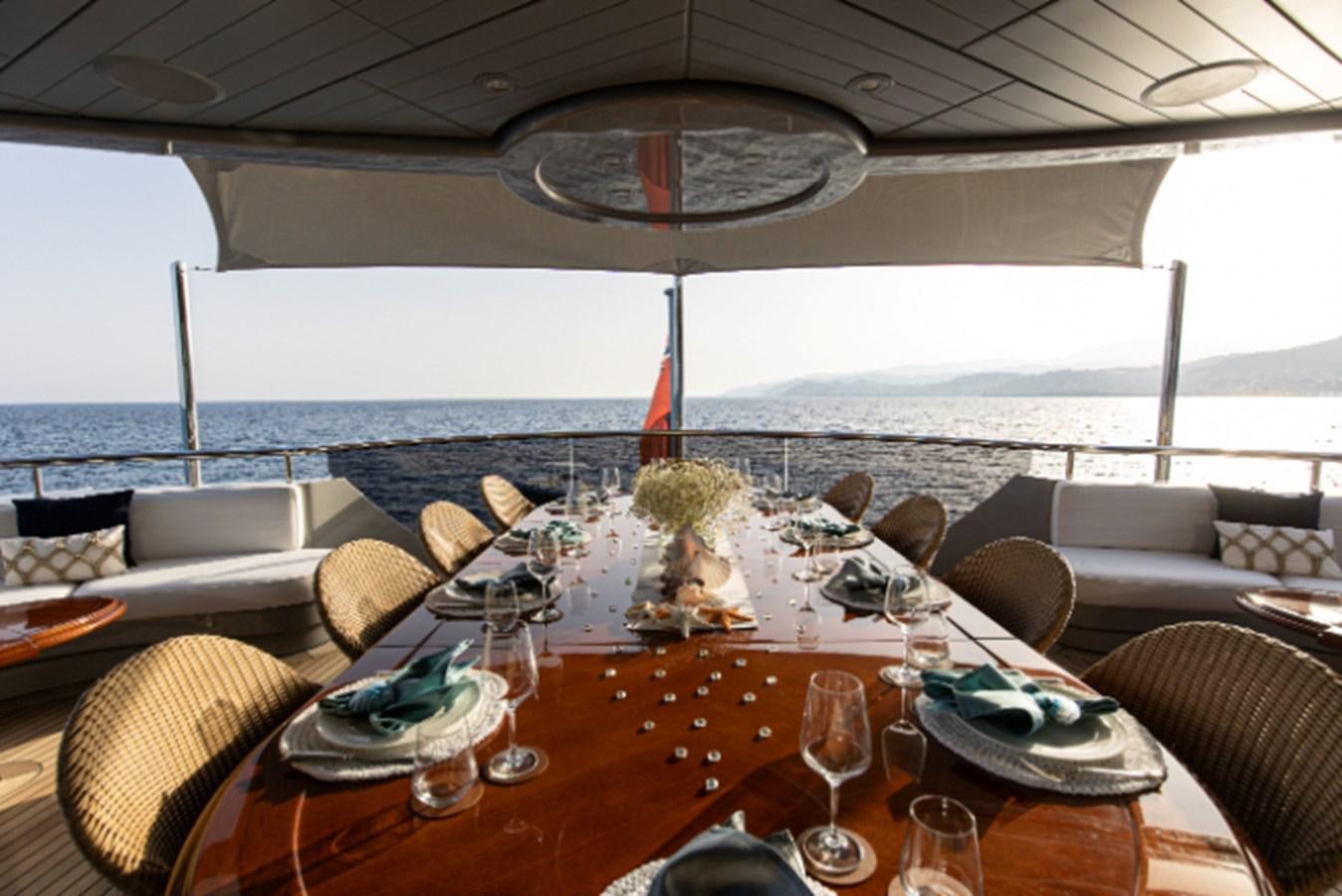 a table with chairs and a large window overlooking a beach aboard VIBRANCE Yacht for Sale