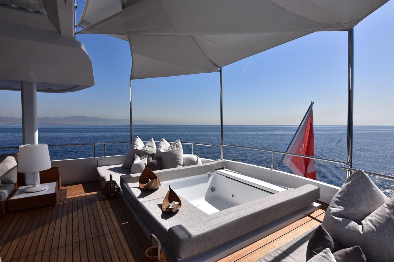 a large white bed with a red and white umbrella on a balcony aboard LIFE SAGA Yacht for Sale