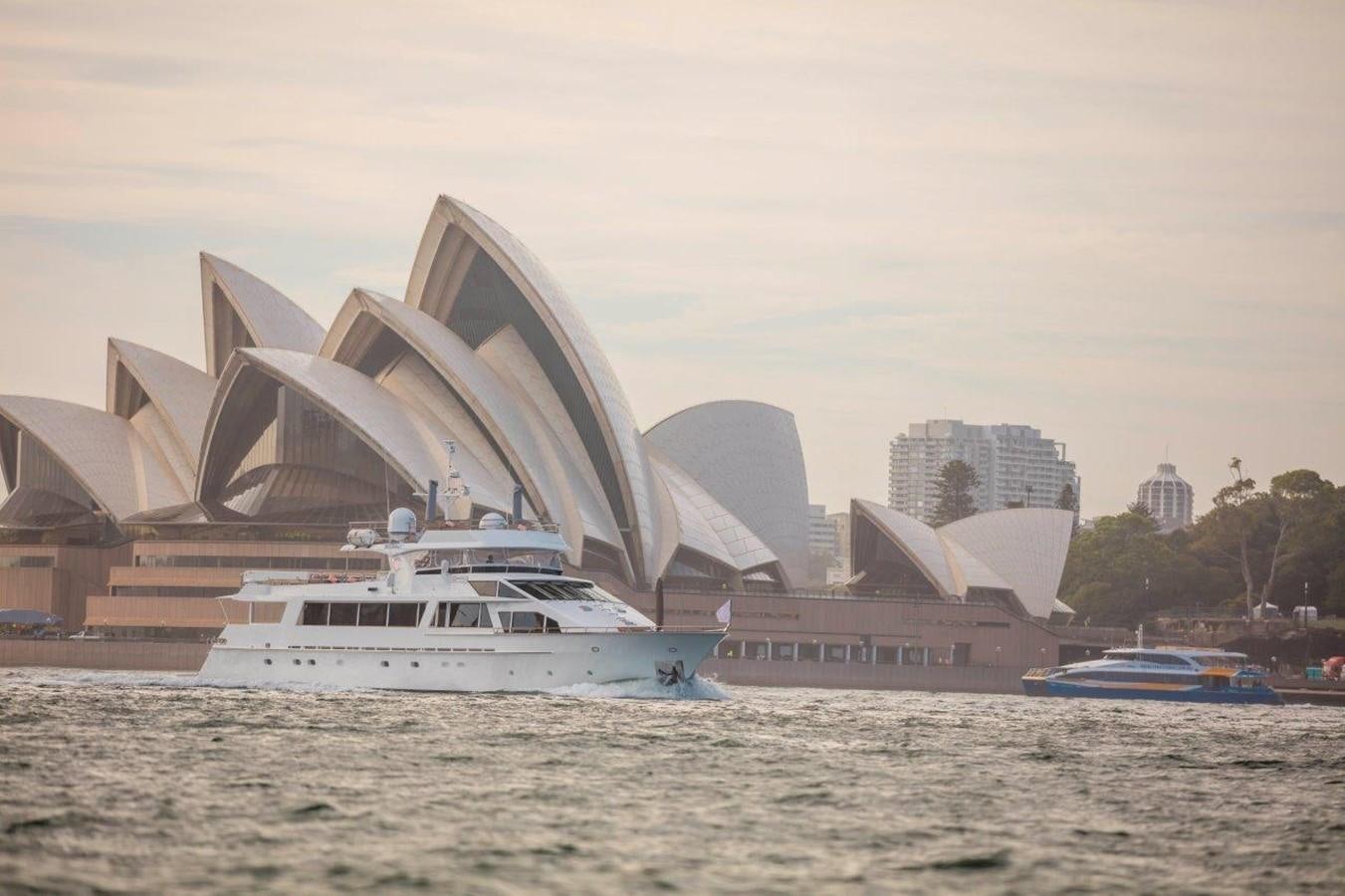 a boat in the water with Sydney Opera House in the background aboard CORROBOREE Yacht for Sale