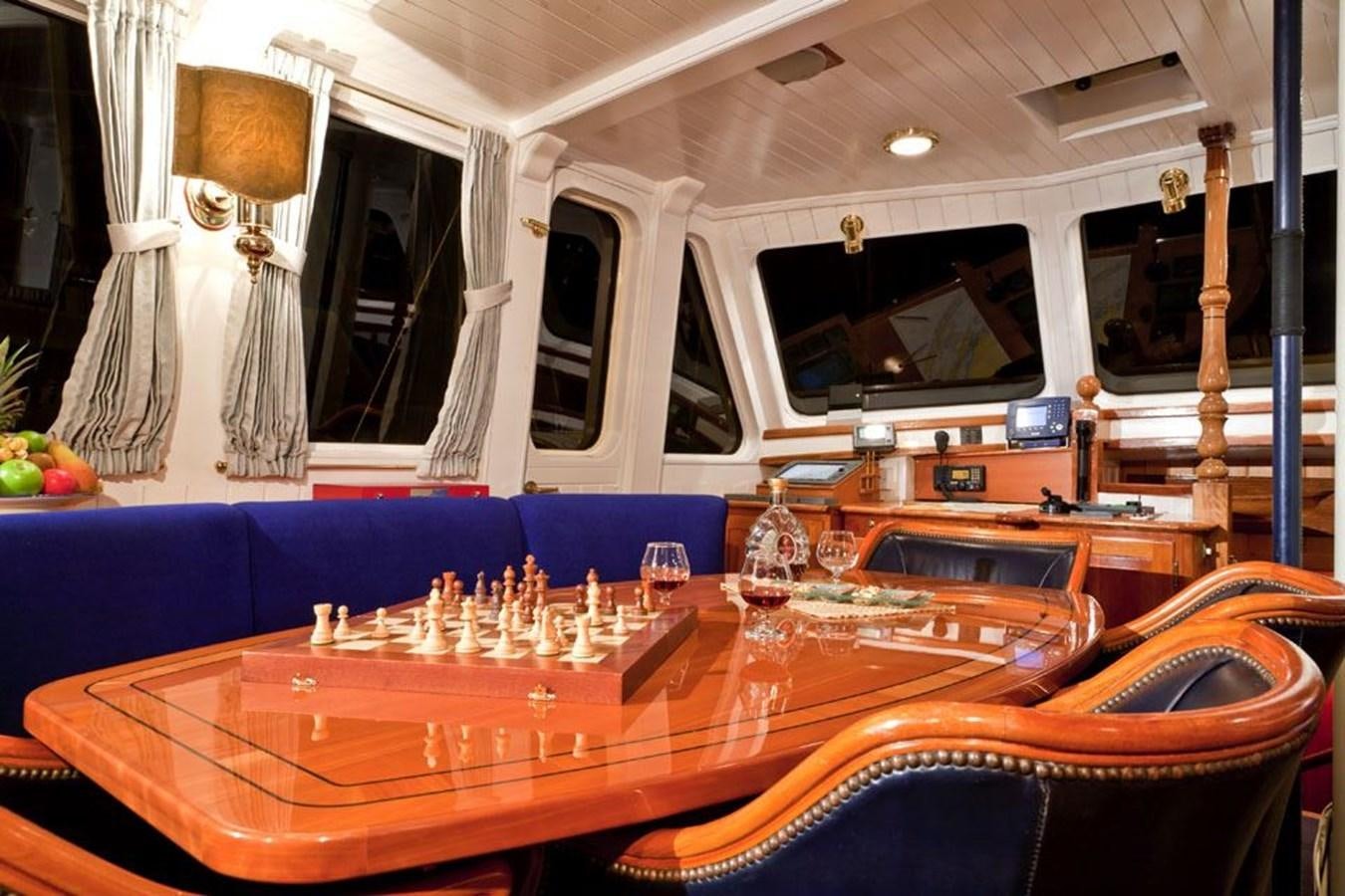 a table with a game board and a chair in a room with a window and curtains aboard TIGERLILY OF CORNWALL Yacht for Sale