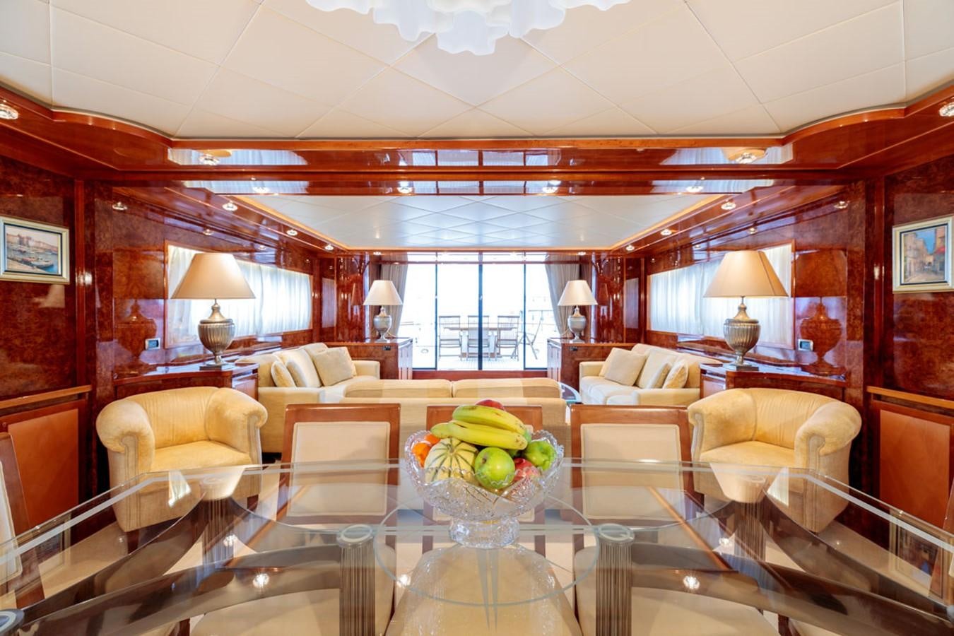a large living room with a large glass table and a large window aboard PARAM JAMUNA III Yacht for Sale