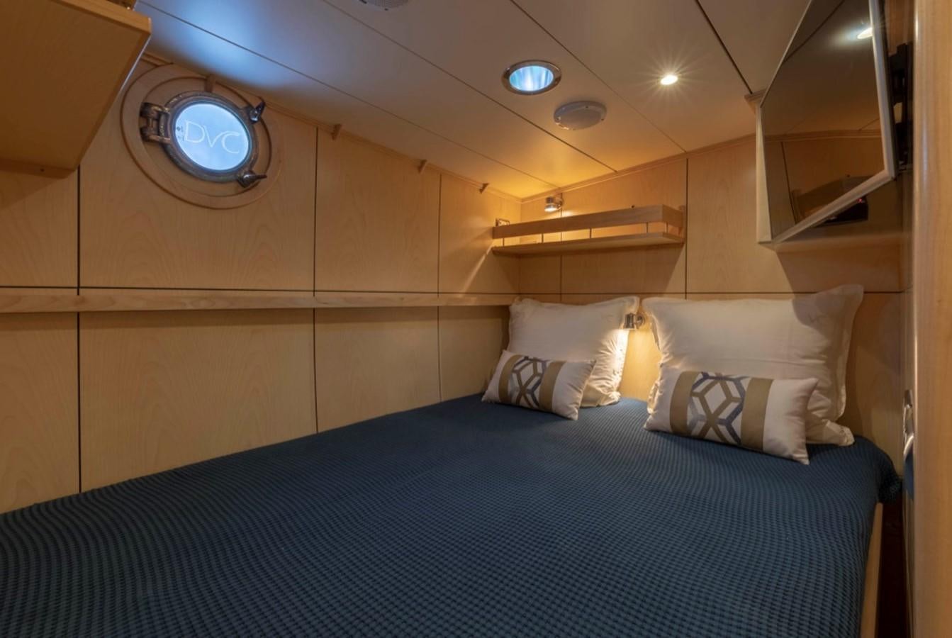 a bed with a blue comforter and a round light aboard DE VROUWE CHRISTINA Yacht for Sale