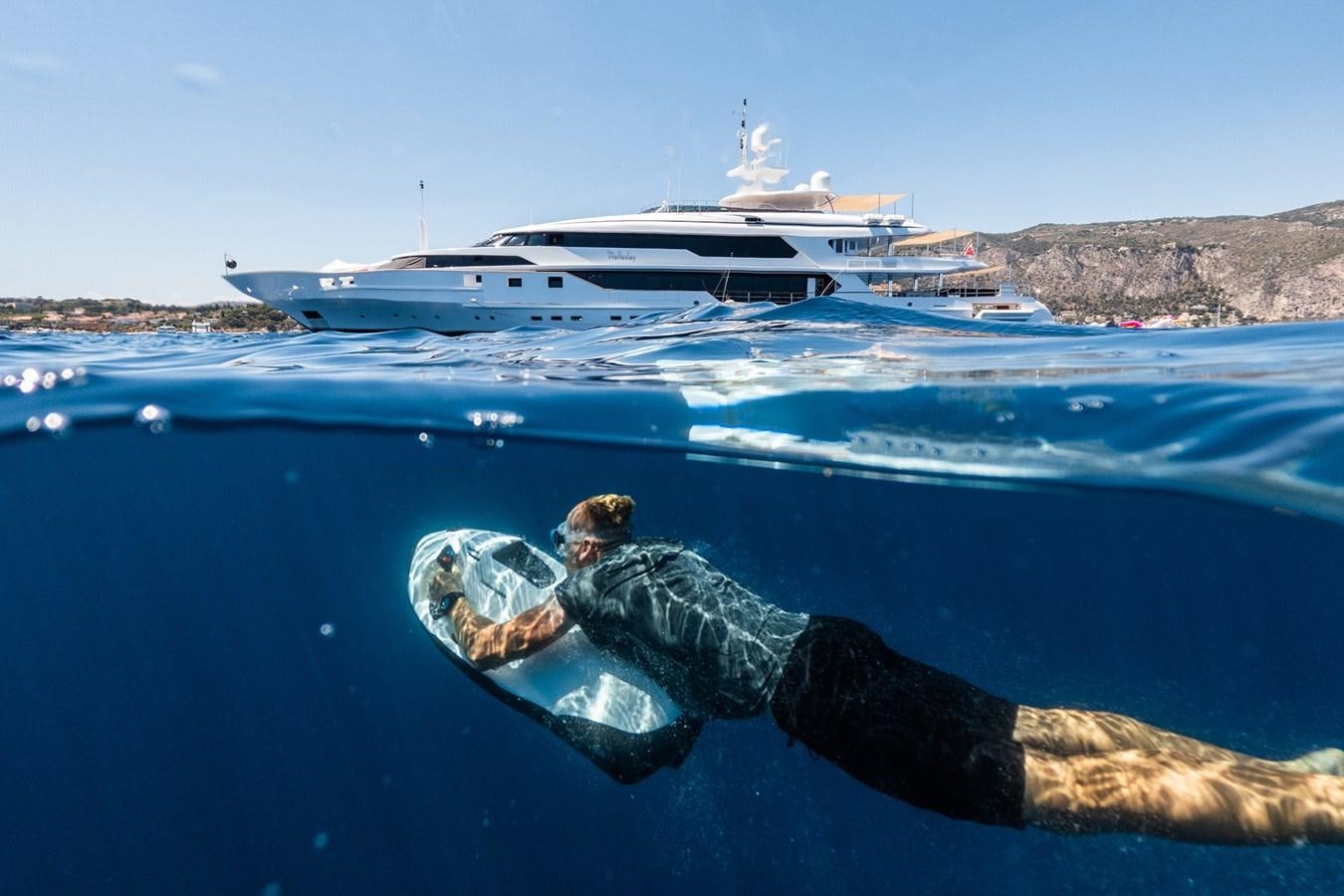 a man lying on a log in the water with a boat in the background aboard THE WELLESLEY Yacht for Sale