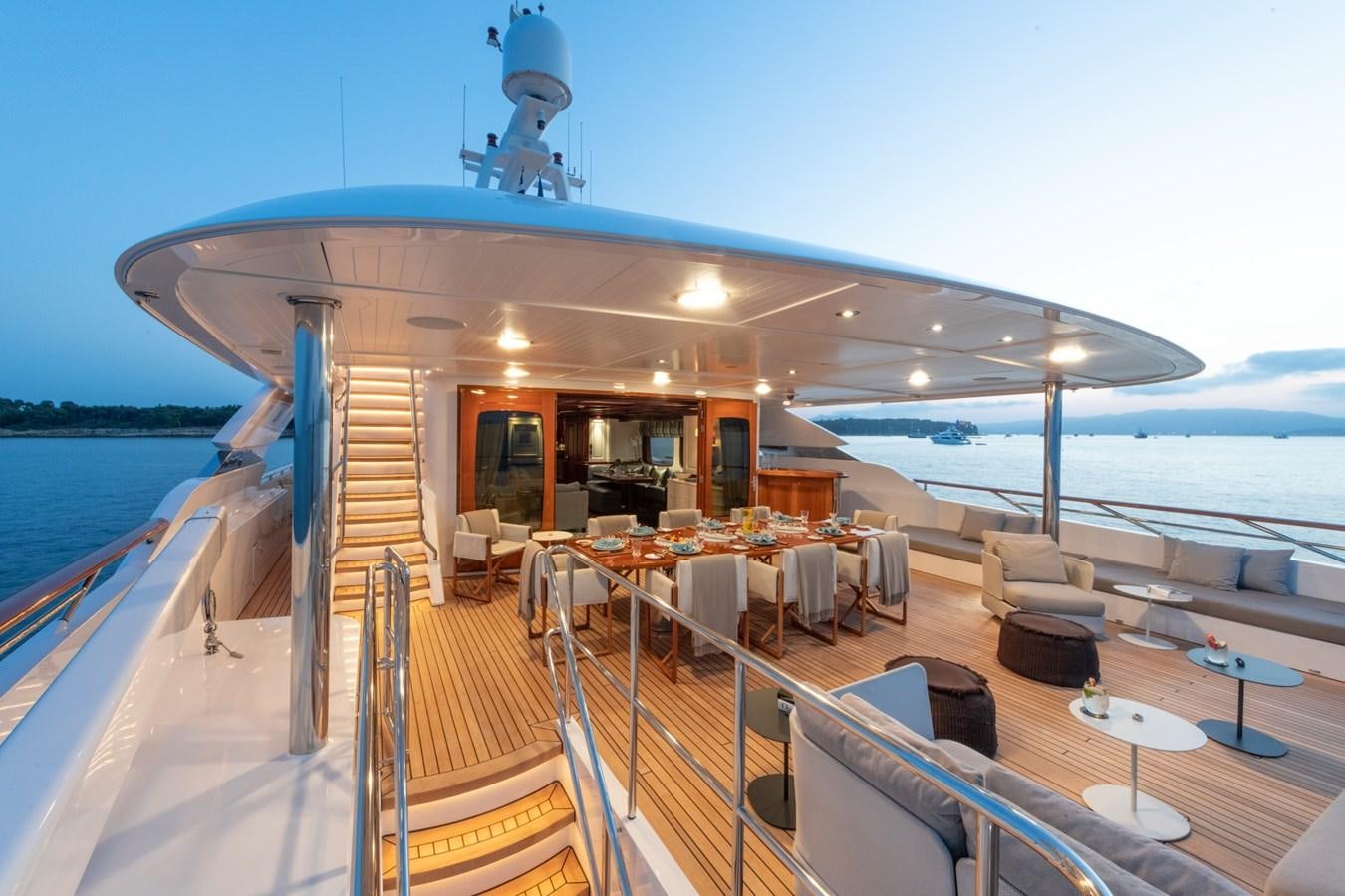 a deck with tables and chairs on it and a body of water in the background aboard AWATEA Yacht for Sale